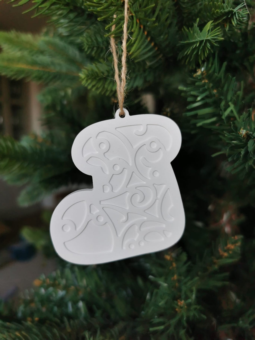 „Weißer Keramik-Baumanhänger in Stiefelform mit ornamentaler Prägung, aufgehängt an einer Juteschnur im Weihnachtsbaum.“
