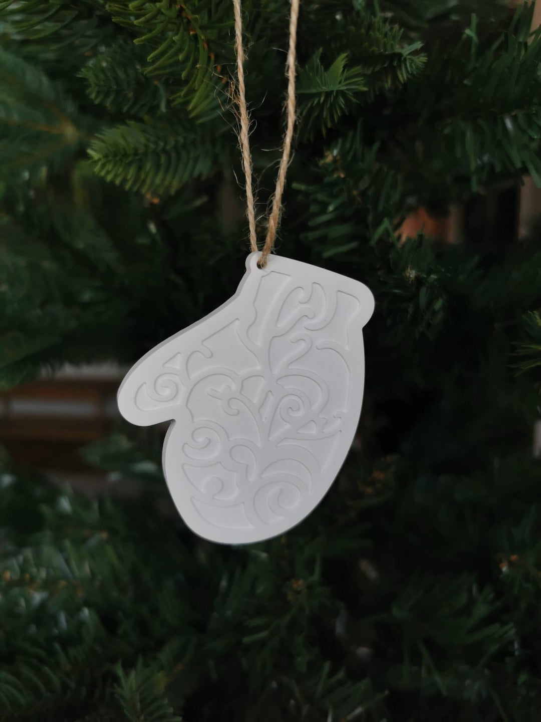 „Weißer Keramik-Weihnachtsanhänger in Handschuhform mit Ornamenten, hängend im grünen Tannenbaum.“