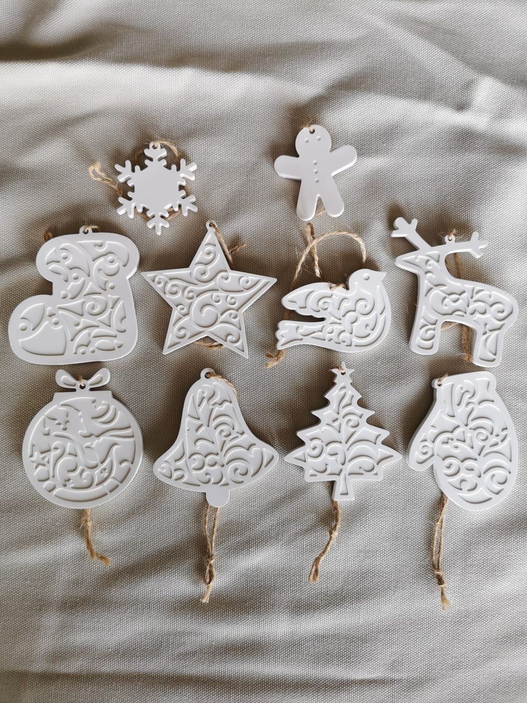 „10 handgefertigte weiße Keramik-Weihnachtsanhänger mit filigranen Ornamenten, liegend präsentiert – Deko für Weihnachtsbaum und Geschenkideen.“