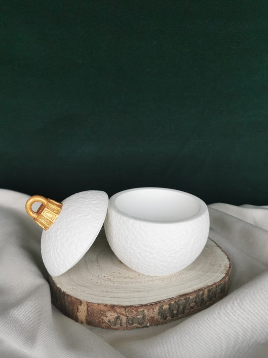 „Schneeweiße Keramikkugel mit goldener Kappe, handgefertigt, mit feiner Struktur und abnehmbarem Deckel – elegante nachhaltige Weihnachtsdekoration auf Holzuntergrund.
