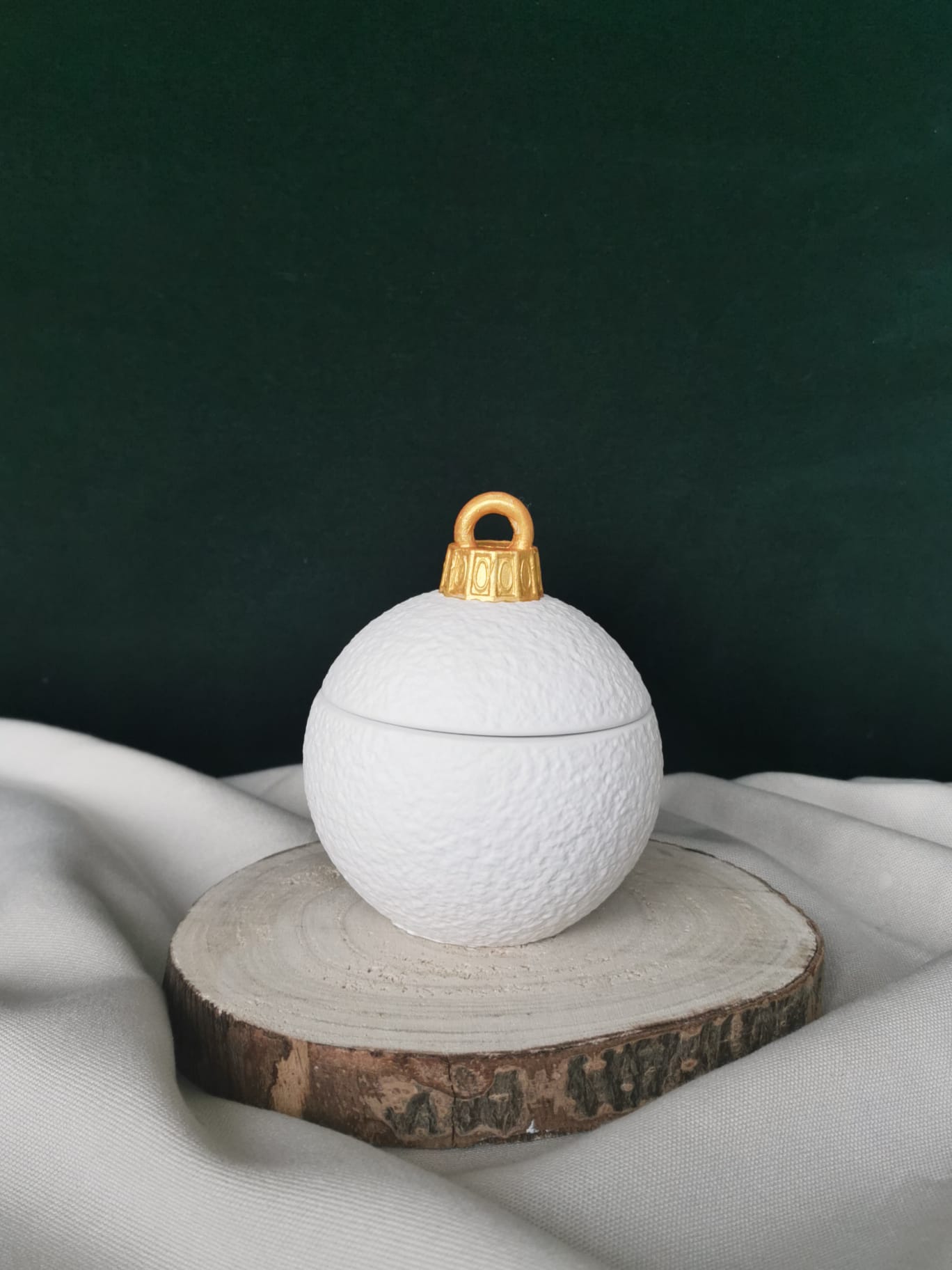 „Schneeweiße Keramikkugel mit goldener Kappe, handgefertigt, mit feiner Struktur und abnehmbarem Deckel – elegante nachhaltige Weihnachtsdekoration auf Holzuntergrund.