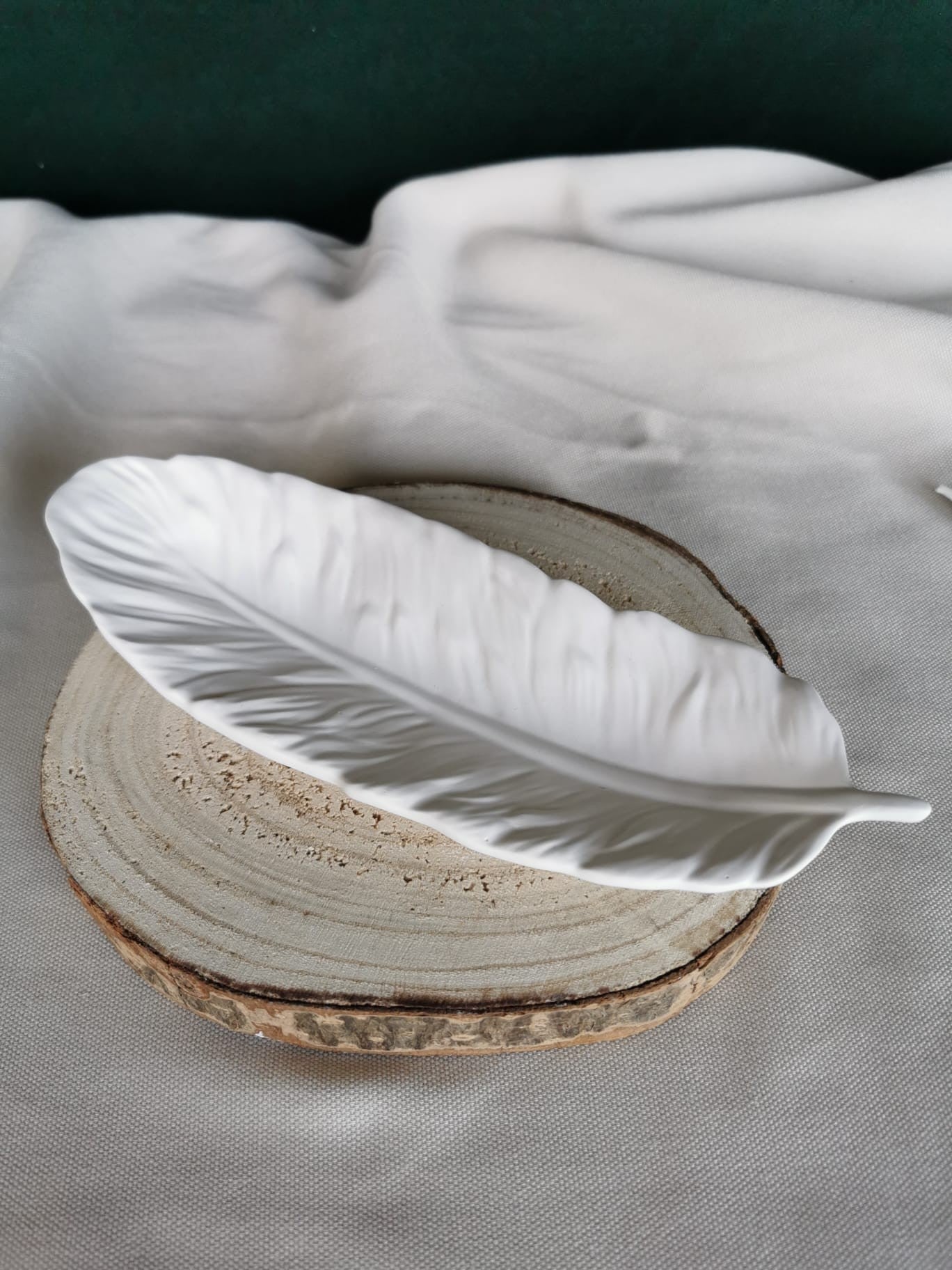 Weiße, handgefertigte Keramikschale in Federform mit feiner Struktur, auf Holzuntergrund platziert – elegante Dekoschale oder Ablagetablett für moderne Wohnräume