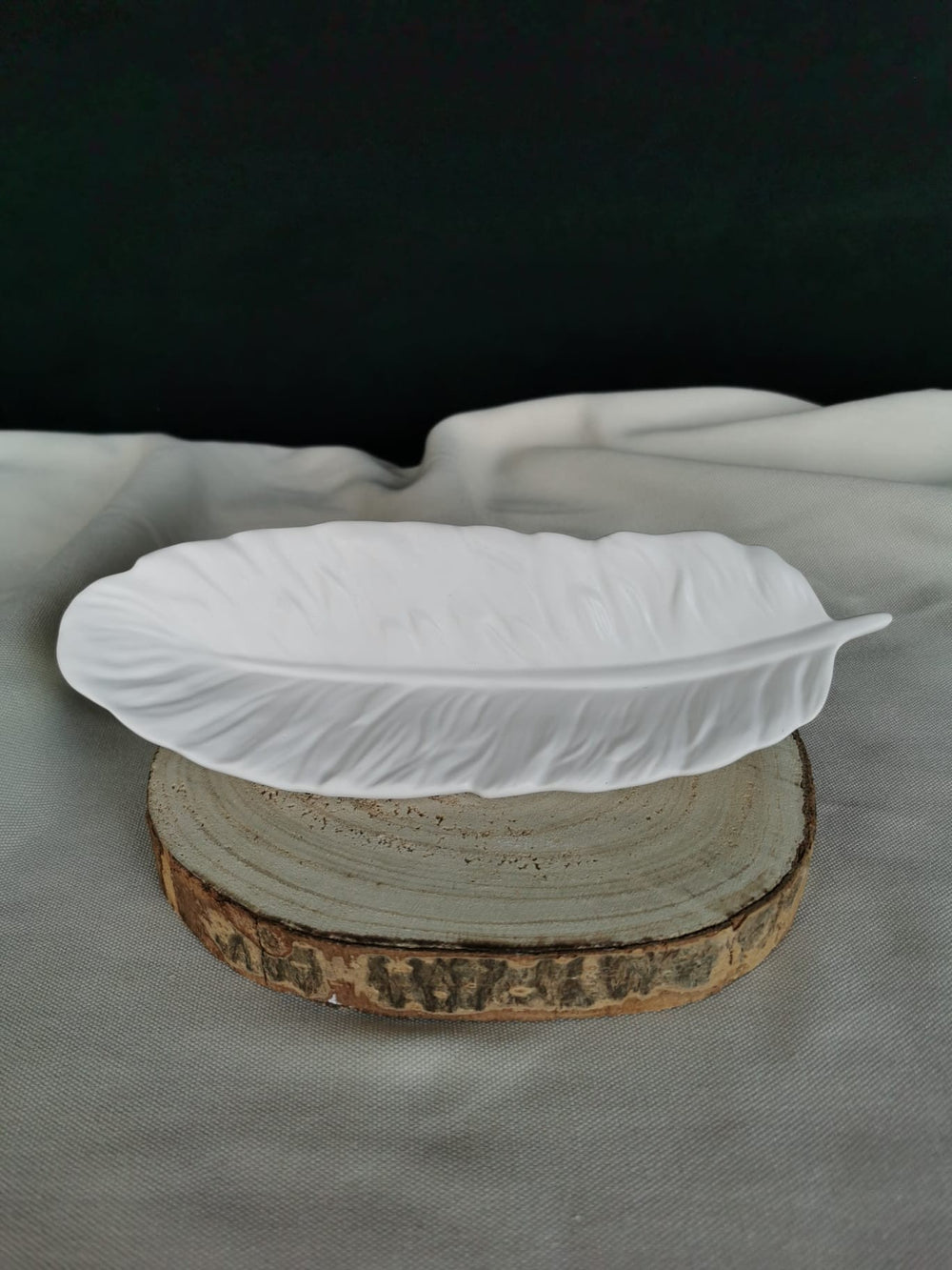 Weiße, handgefertigte Keramikschale in Federform mit feiner Struktur, auf Holzuntergrund platziert – elegante Dekoschale oder Ablagetablett für moderne Wohnräume