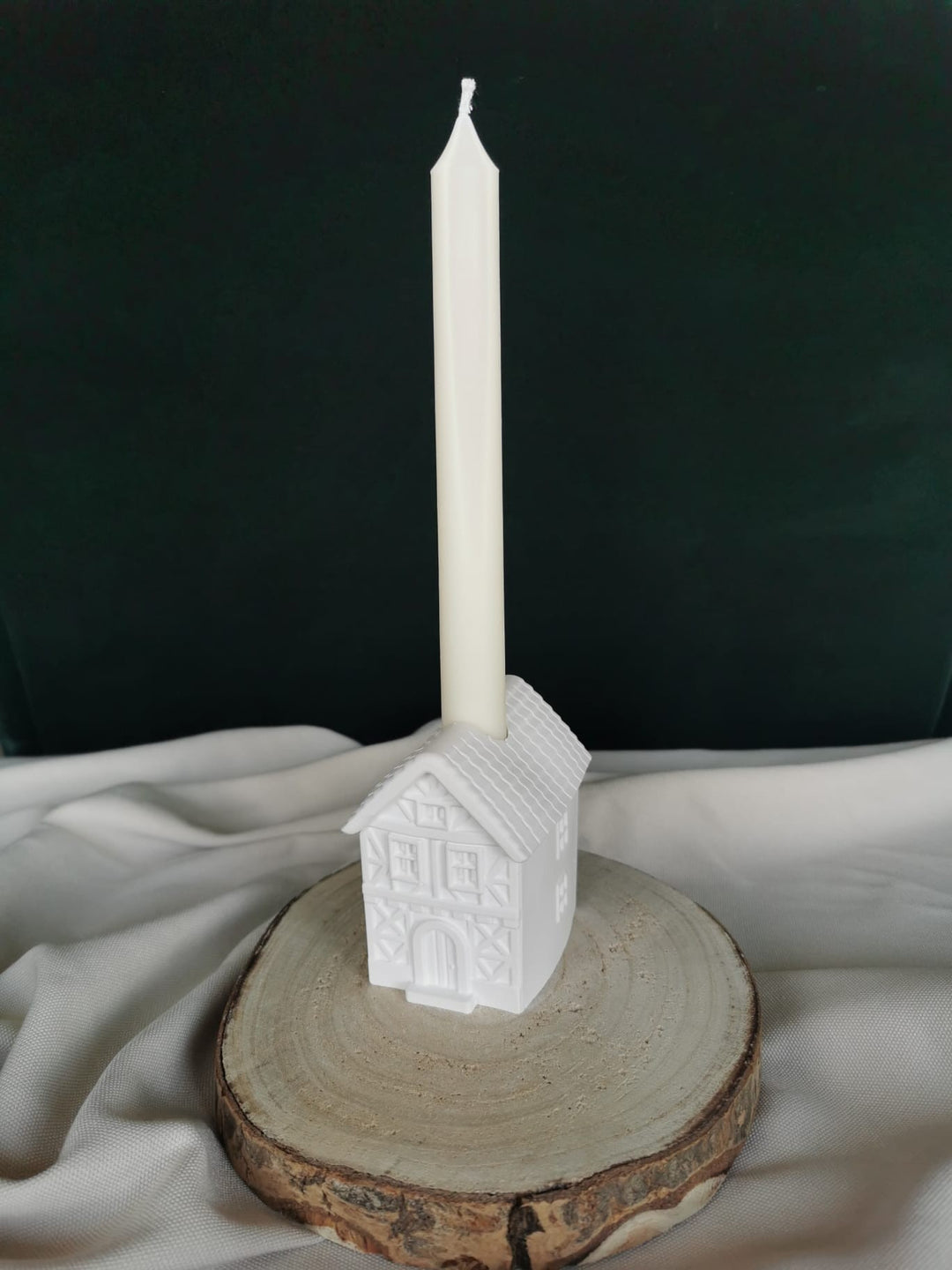 „Weißer Kerzenhalter in Form eines Fachwerkhauses aus Gips, handgefertigte Weihnachtsdekoration auf Holzbrett präsentiert.“