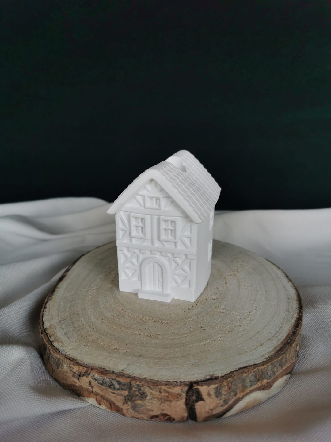 „Weißer Kerzenhalter in Form eines Fachwerkhauses aus Gips, handgefertigte Weihnachtsdekoration auf Holzbrett präsentiert.“