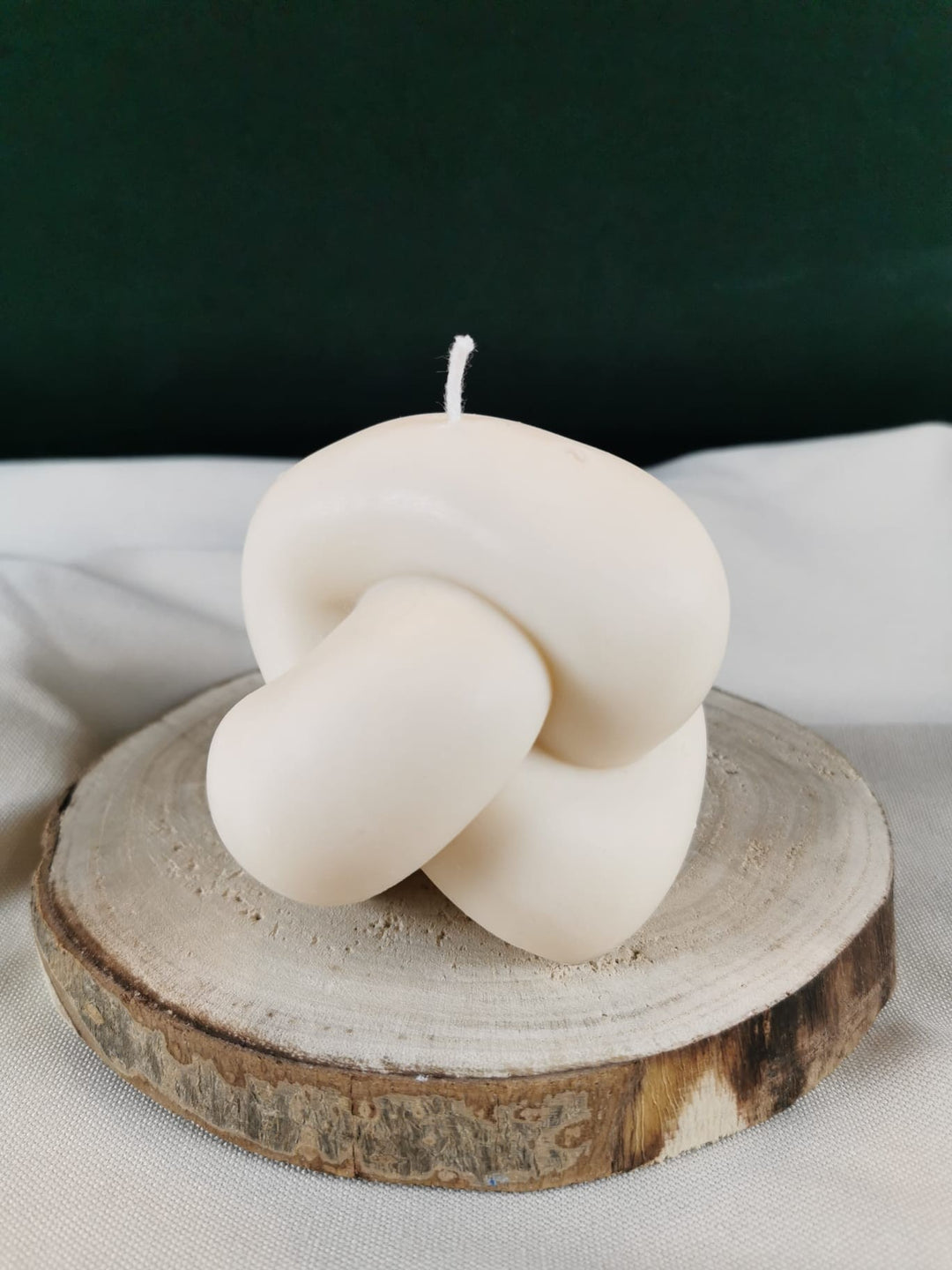 Handgegossene Knot-Kerze aus weißem Bio-Rapswachs, dekorativ auf einer Holzscheibe präsentiert.