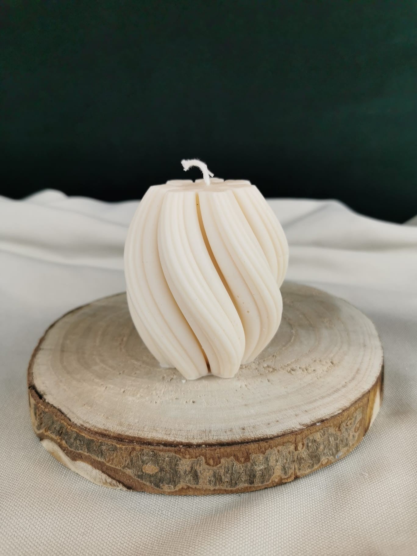 Handgegossene runde Twist Kugelkerze aus natürlichem Rapswachs in elegant gedrehtem Design, dekorativ auf Holzscheibe platziert.