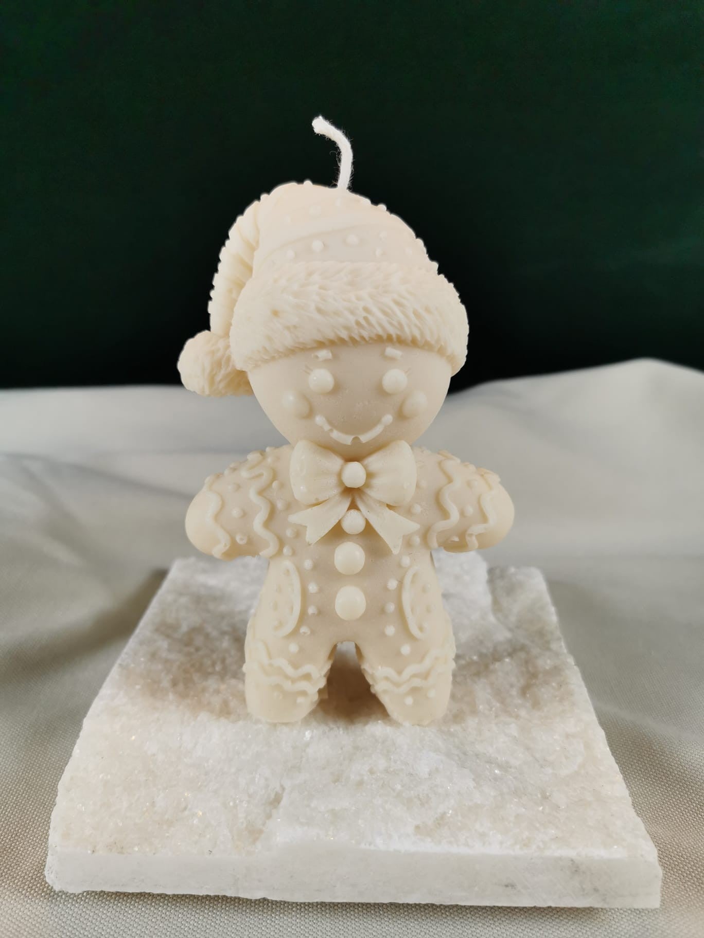 Handgegossene Lebkuchen-Figurenkerze aus hellem Rapswachs, mit Mütze, Schleife und detailliertem Muster, auf einer hellen Steinplatte präsentiert.