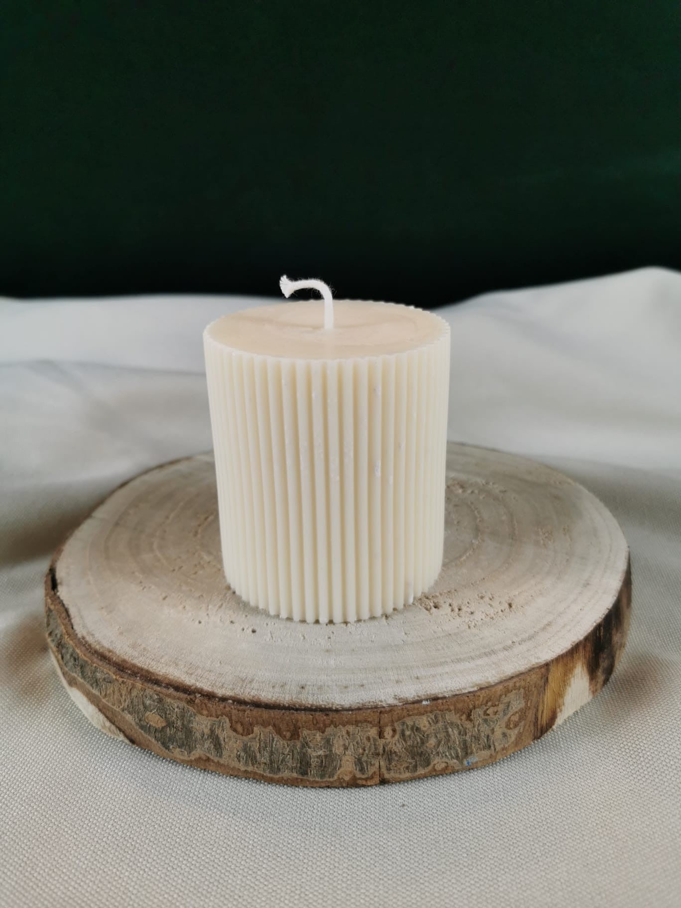 „Kleine gerillte Stumpenkerze aus Rapswachs in Cremeweiß auf Holzunterlage.“