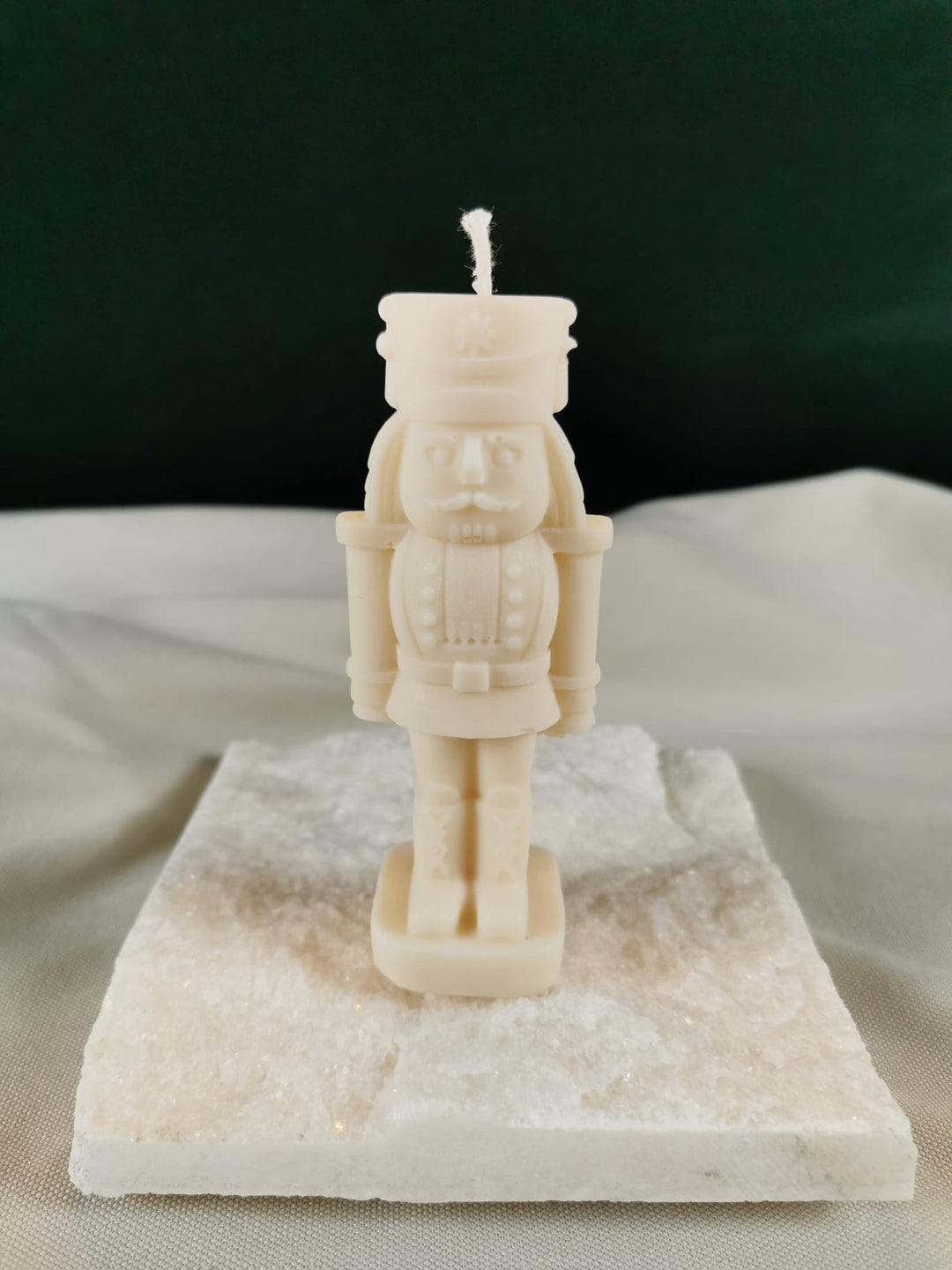 Handgegossene Nussknacker-Figurenkerze aus hellem Rapswachs, detailliert gestaltet in klassischer Form, präsentiert auf einer glänzenden Steinplatte.
