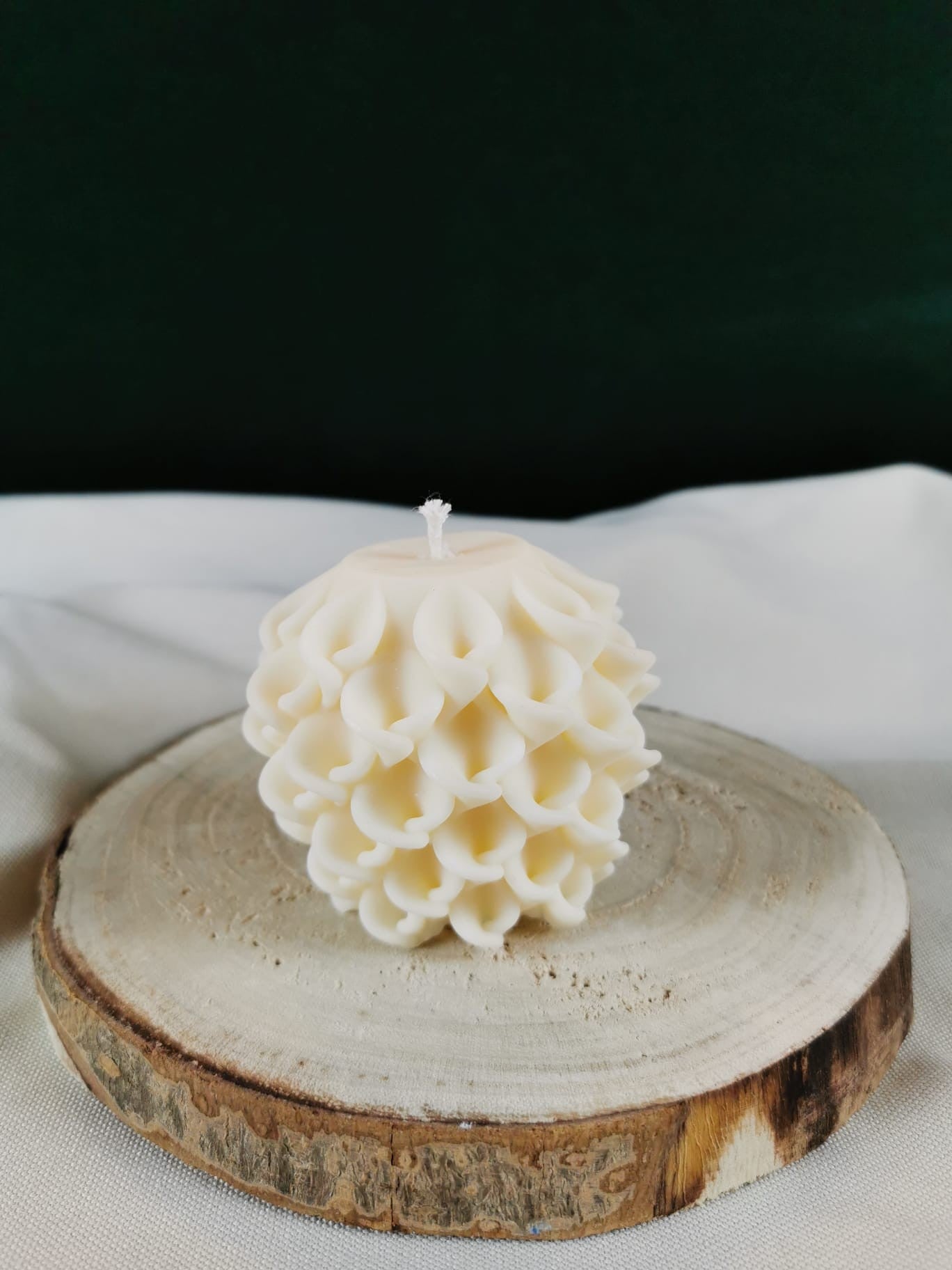 Handgegossene cremeweiße Ornament-Kugelkerze aus Rapswachs auf Steinplatte – weihnachtliche Dekoration.