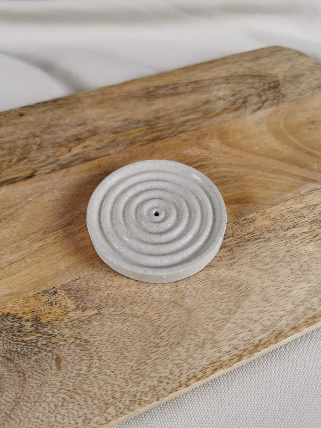 „Handgefertigter runder Beton-Räucherstäbchenhalter mit kreisförmiger Struktur auf Holzunterlage.“