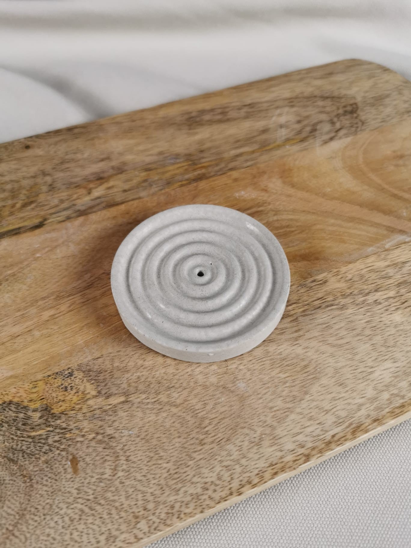 „Handgefertigter runder Beton-Räucherstäbchenhalter mit kreisförmiger Struktur auf Holzunterlage.“