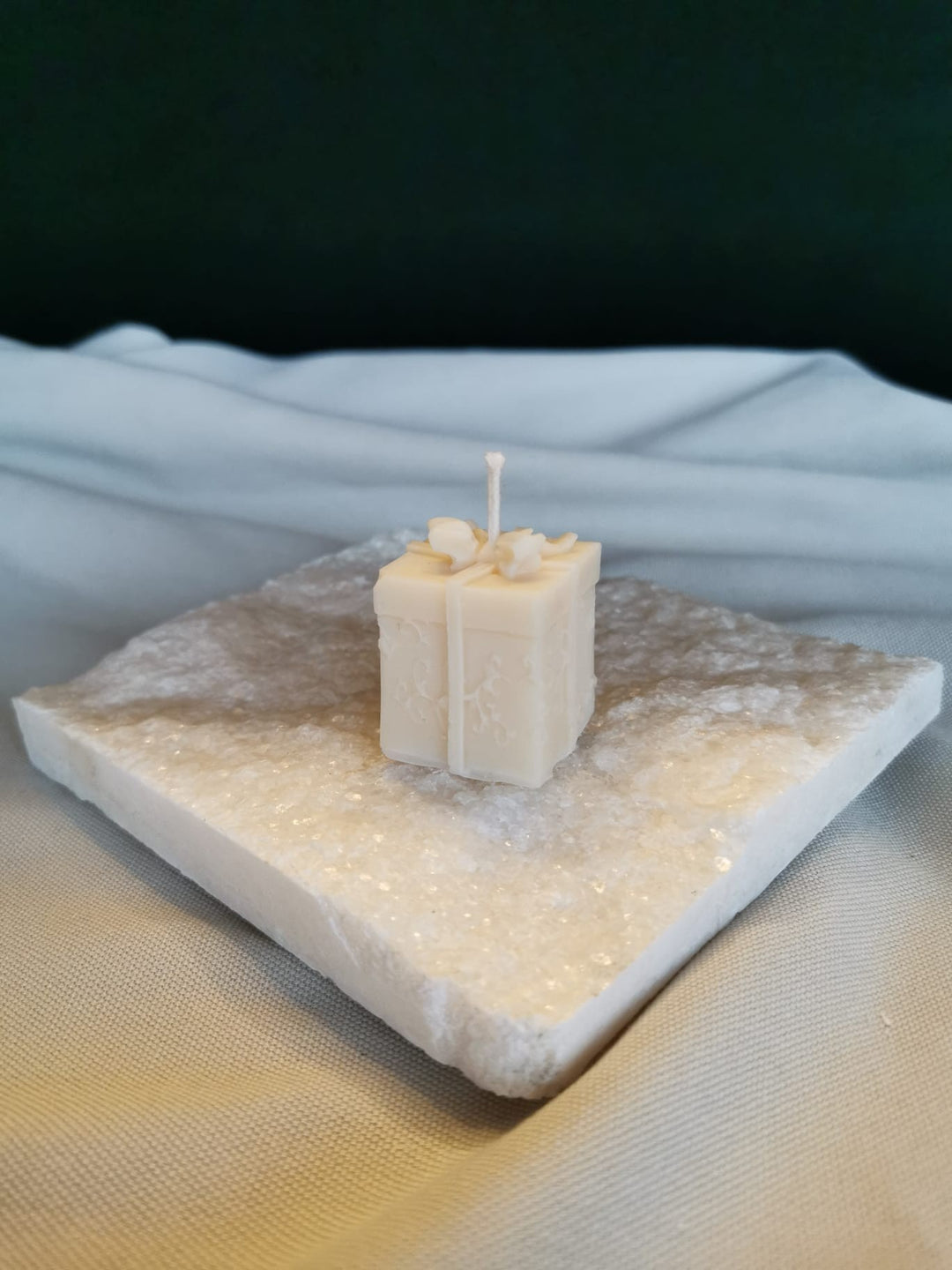 „Handgemachte Geschenk-Kerze aus cremigem Rapswachs in Geschenkbox-Form, dekorativ präsentiert auf einer weißen Steinplatte.“