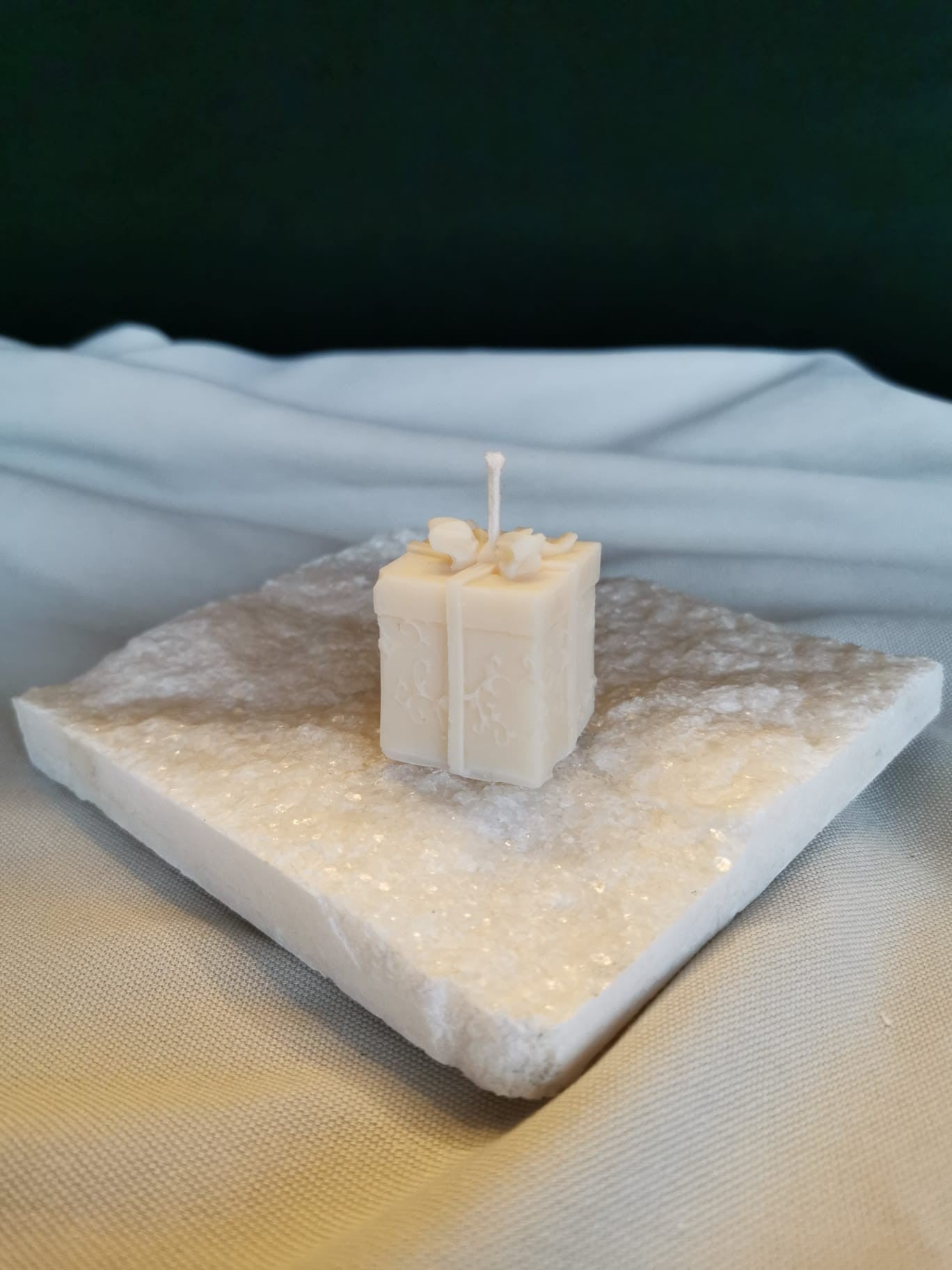 „Handgemachte Geschenk-Kerze aus cremigem Rapswachs in Geschenkbox-Form, dekorativ präsentiert auf einer weißen Steinplatte.“