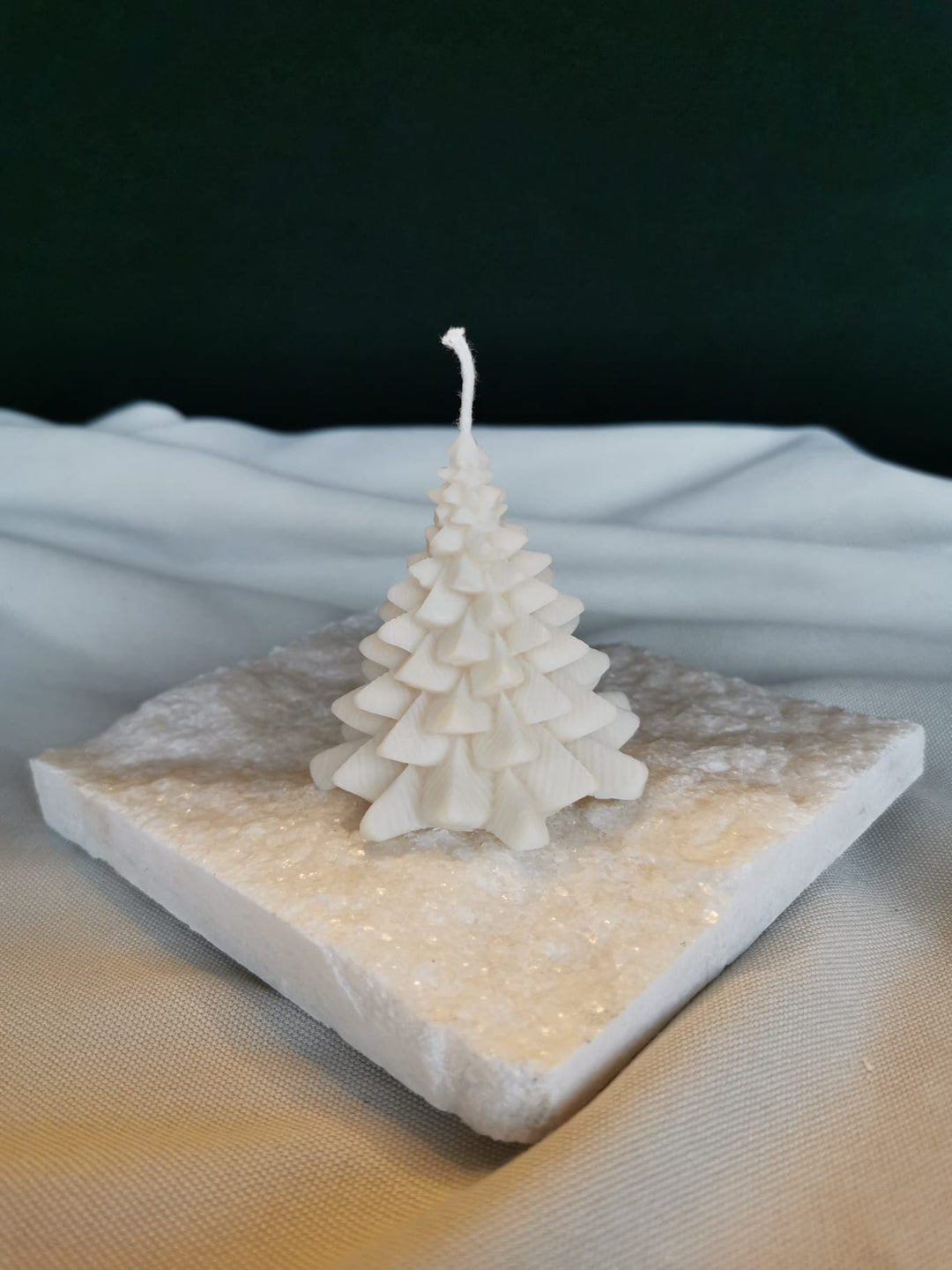 „Handgemachte vegane Rapswachskerze in Form eines kleinen weißen Weihnachtsbaums auf Holzunterlage.“