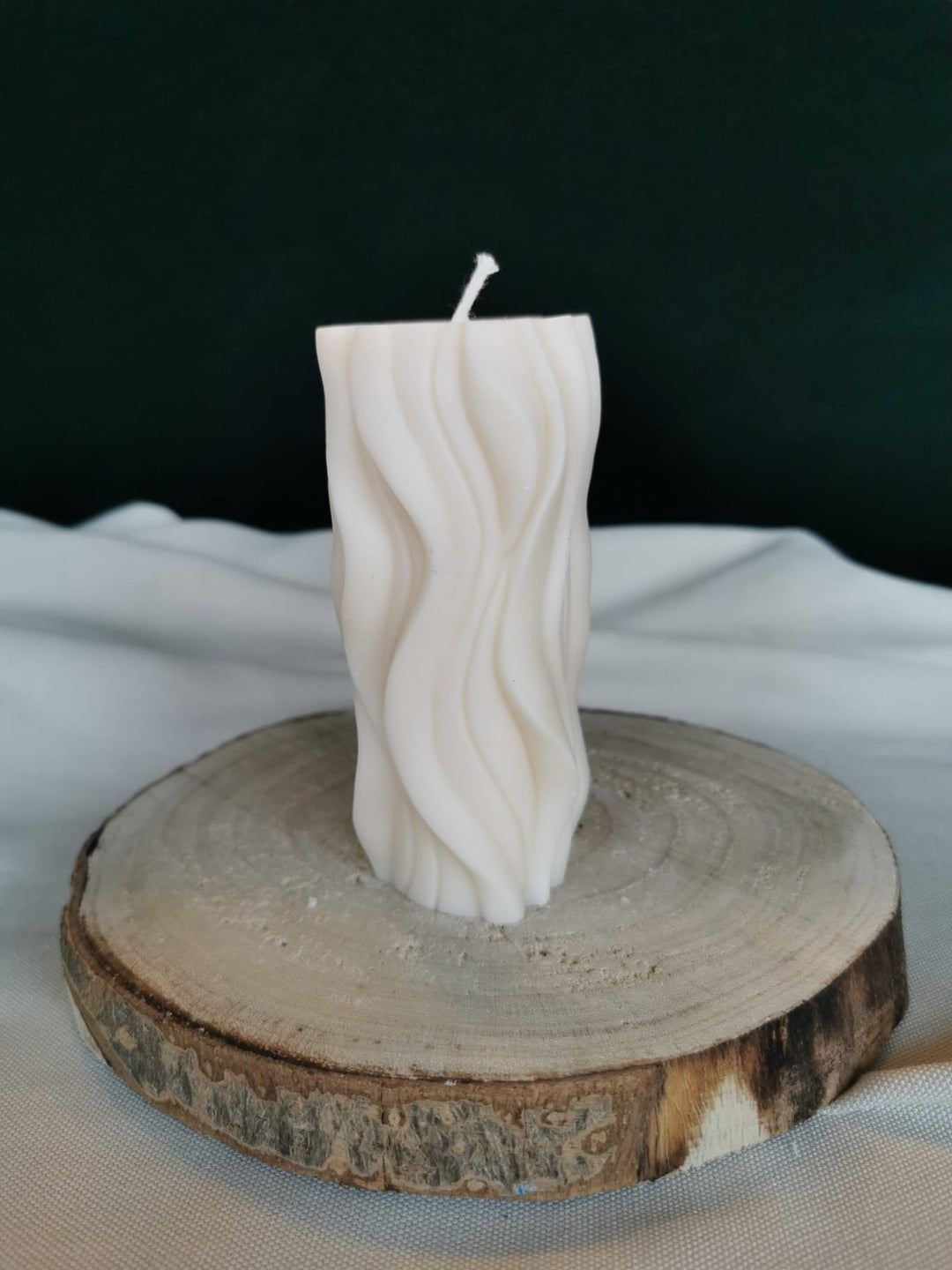 „Handgegossene cremefarbene Rapswachskerze im modernen Wellen-Design auf rustikalem Holzuntergrund – nachhaltige vegane Deko-Kerze.“