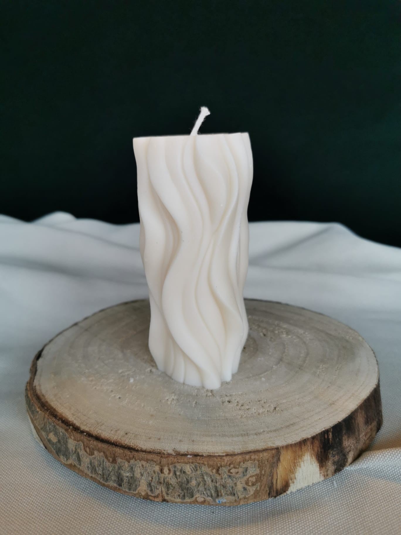 „Handgegossene cremefarbene Rapswachskerze im modernen Wellen-Design auf rustikalem Holzuntergrund – nachhaltige vegane Deko-Kerze.“