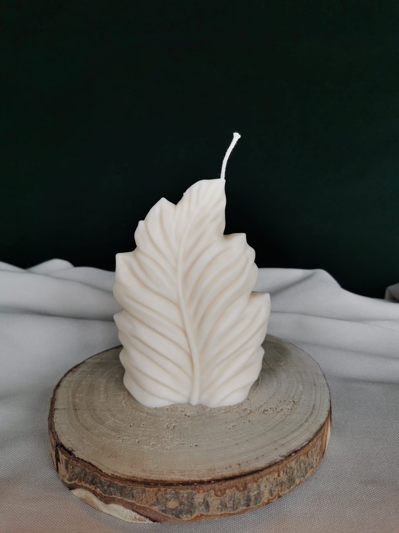 „Handgegossene Rapswachskerze im organischen Blattdesign, stehend auf einer Holzscheibe“