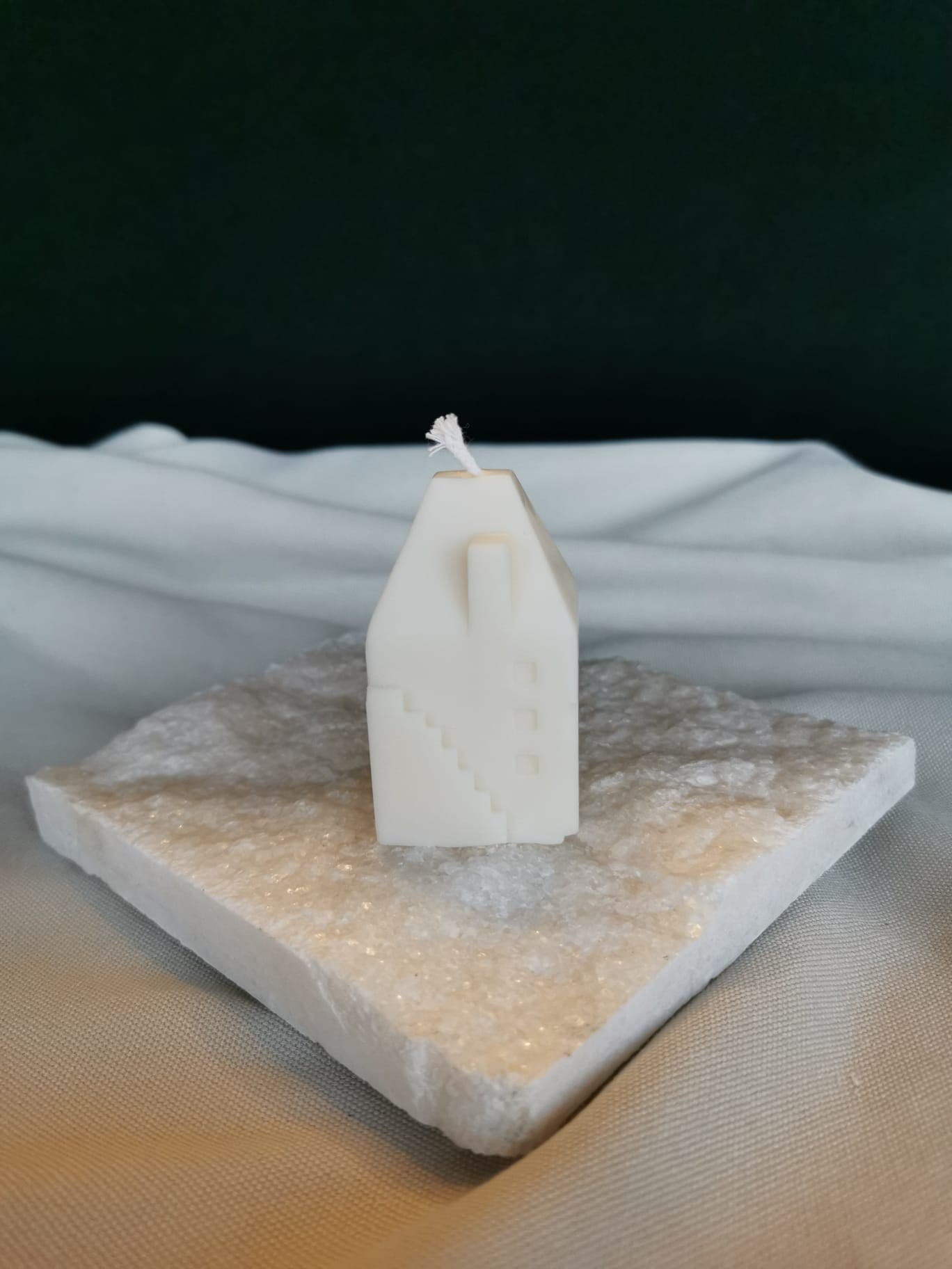 „Handgemachte Rapswachskerze in Form eines kleinen Hauses mit Treppe, auf weißer Unterlage dekoriert.“