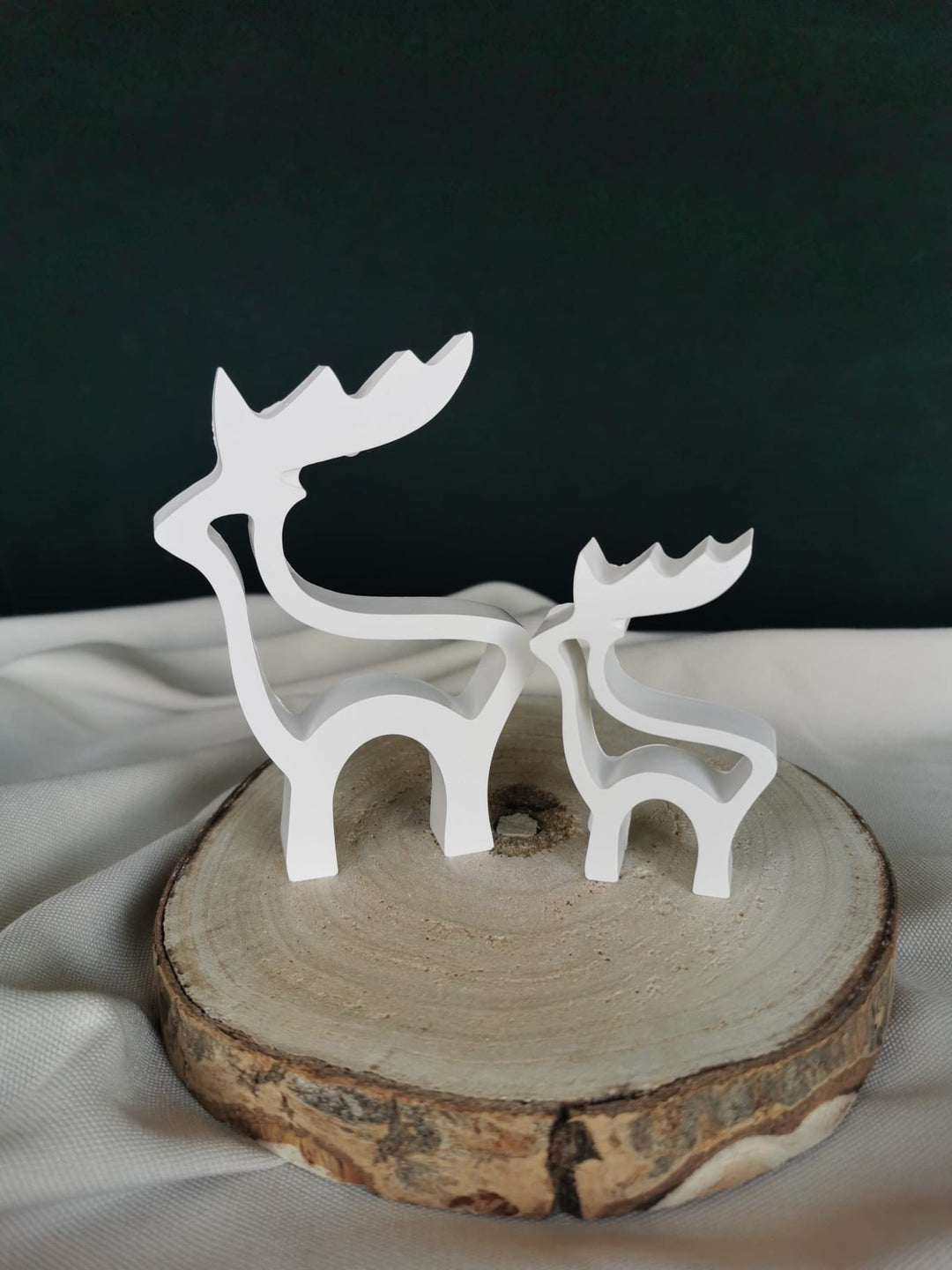 Zwei weiße Rentier-Figuren aus Gießkeramik in offener Silhouettenform, dekorativ auf einer Holzscheibe arrangiert – minimalistische Weihnachtsdeko.