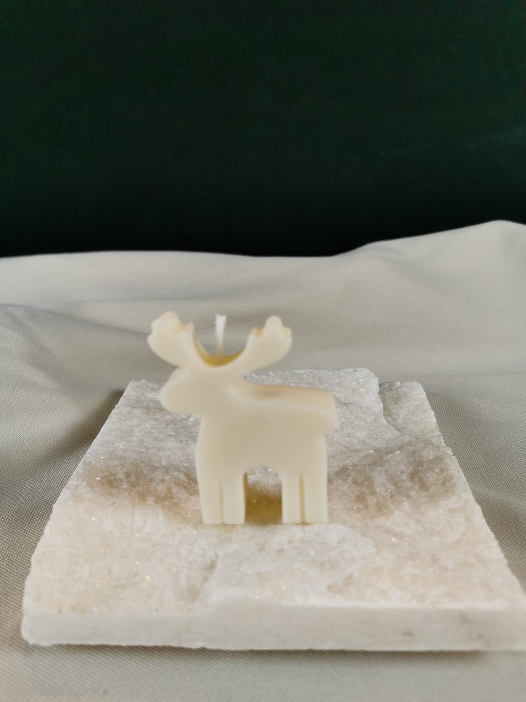 Minimalistische Rentier-Figurenkerze aus hellem Rapswachs mit schlichten Konturen, stehend auf einer glitzernden Steinplatte.