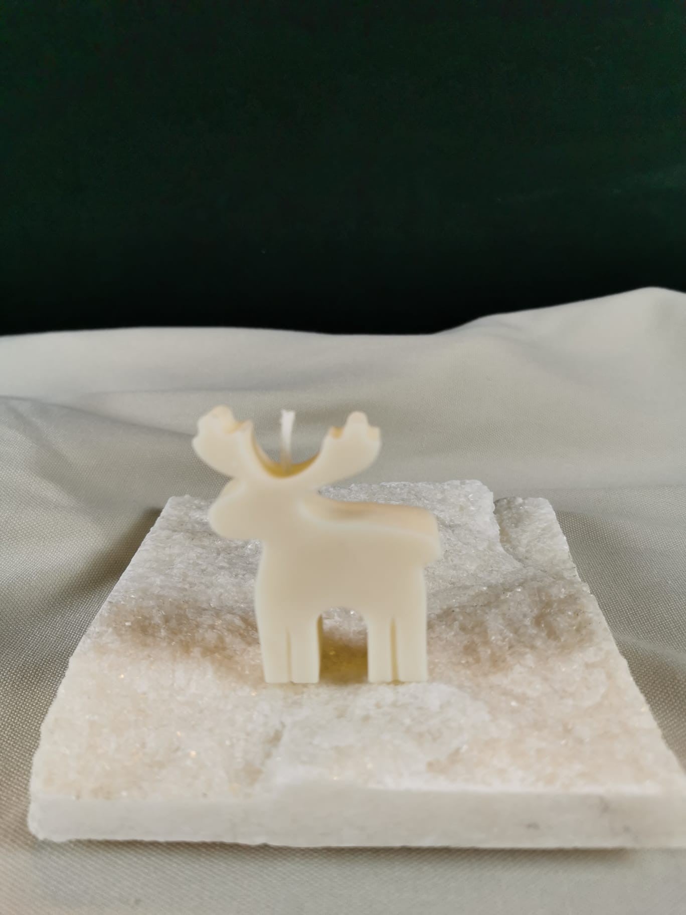 Minimalistische Rentier-Figurenkerze aus hellem Rapswachs mit schlichten Konturen, stehend auf einer glitzernden Steinplatte.