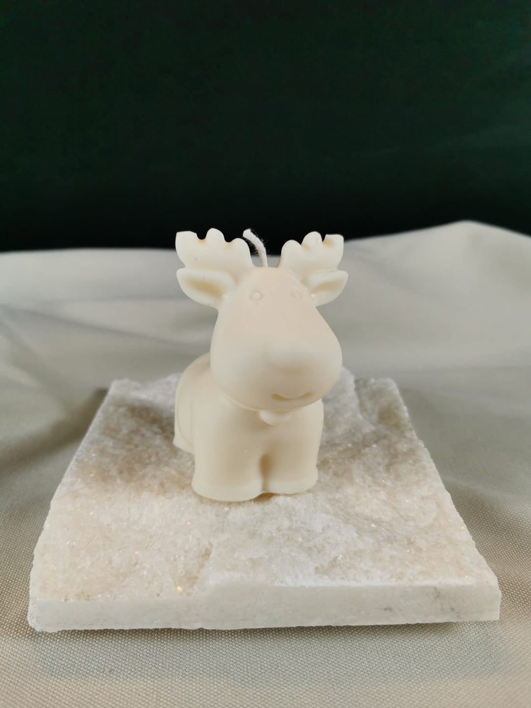 Handgegossene Rentier-Figurenkerze aus hellem Rapswachs, mit großen Geweihen und niedlichem Gesichtsausdruck, dekorativ auf einer hellen Steinplatte platziert.