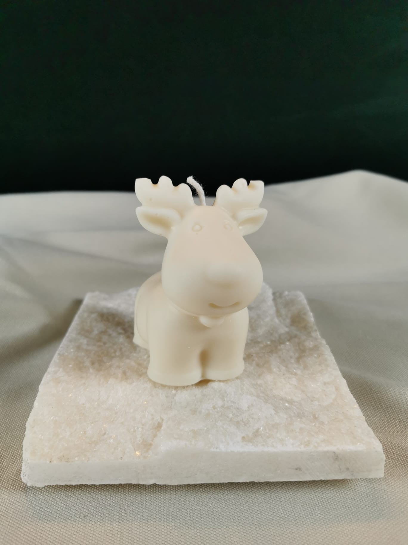 Handgegossene Rentier-Figurenkerze aus hellem Rapswachs, mit großen Geweihen und niedlichem Gesichtsausdruck, dekorativ auf einer hellen Steinplatte platziert.