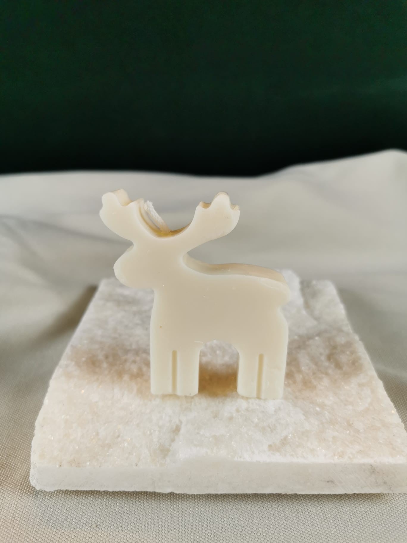 Handgegossene Rentier-Figurenkerze aus hellem Rapswachs in minimalistischer Silhouettenform, stehend auf einer glitzernden Steinplatte.