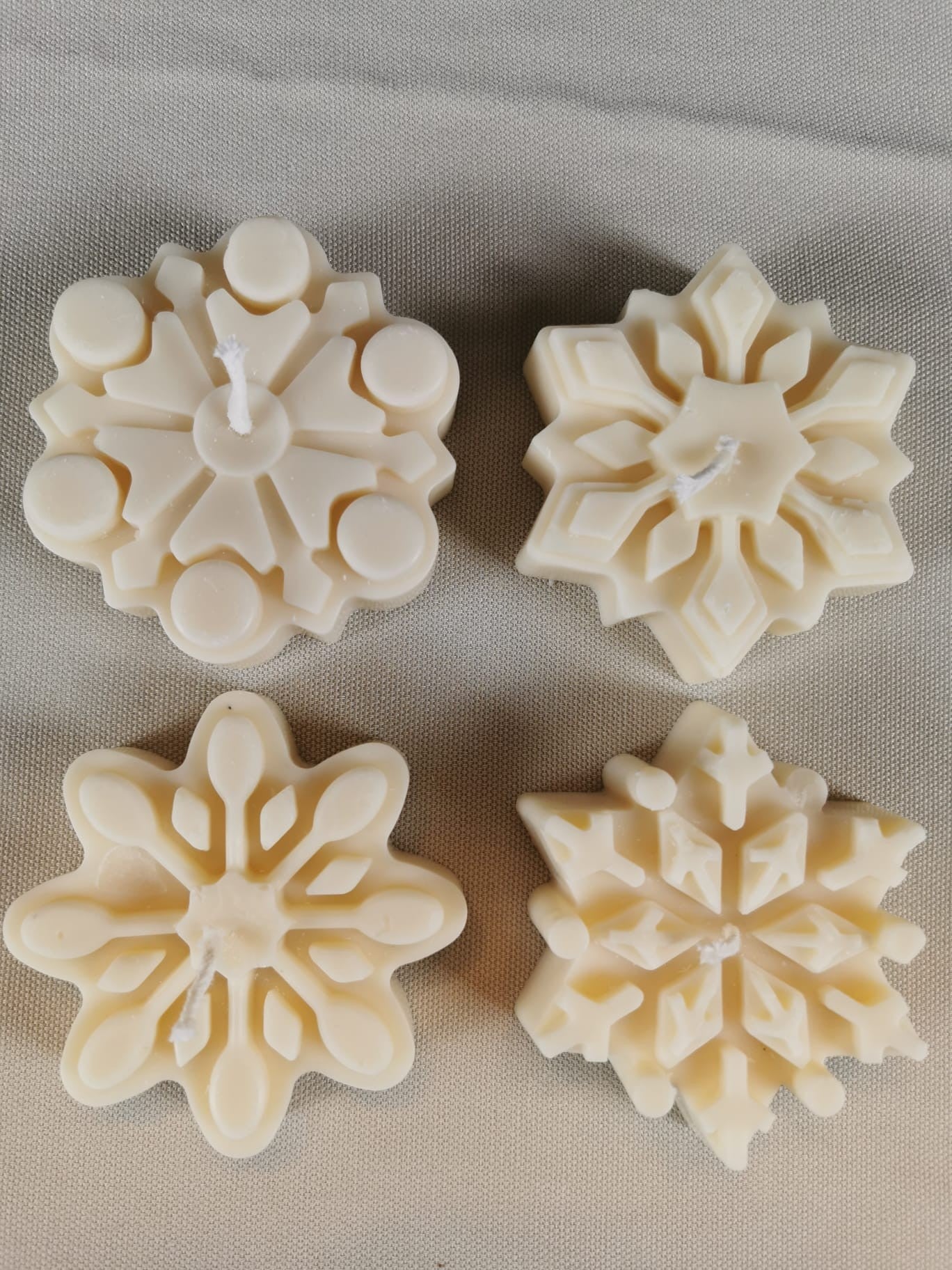 „Handgemachte cremefarbene Schneeflocken-Kerze aus Rapswachs mit feinen winterlichen Details, dekorativ auf hellem Untergrund fotografiert.“