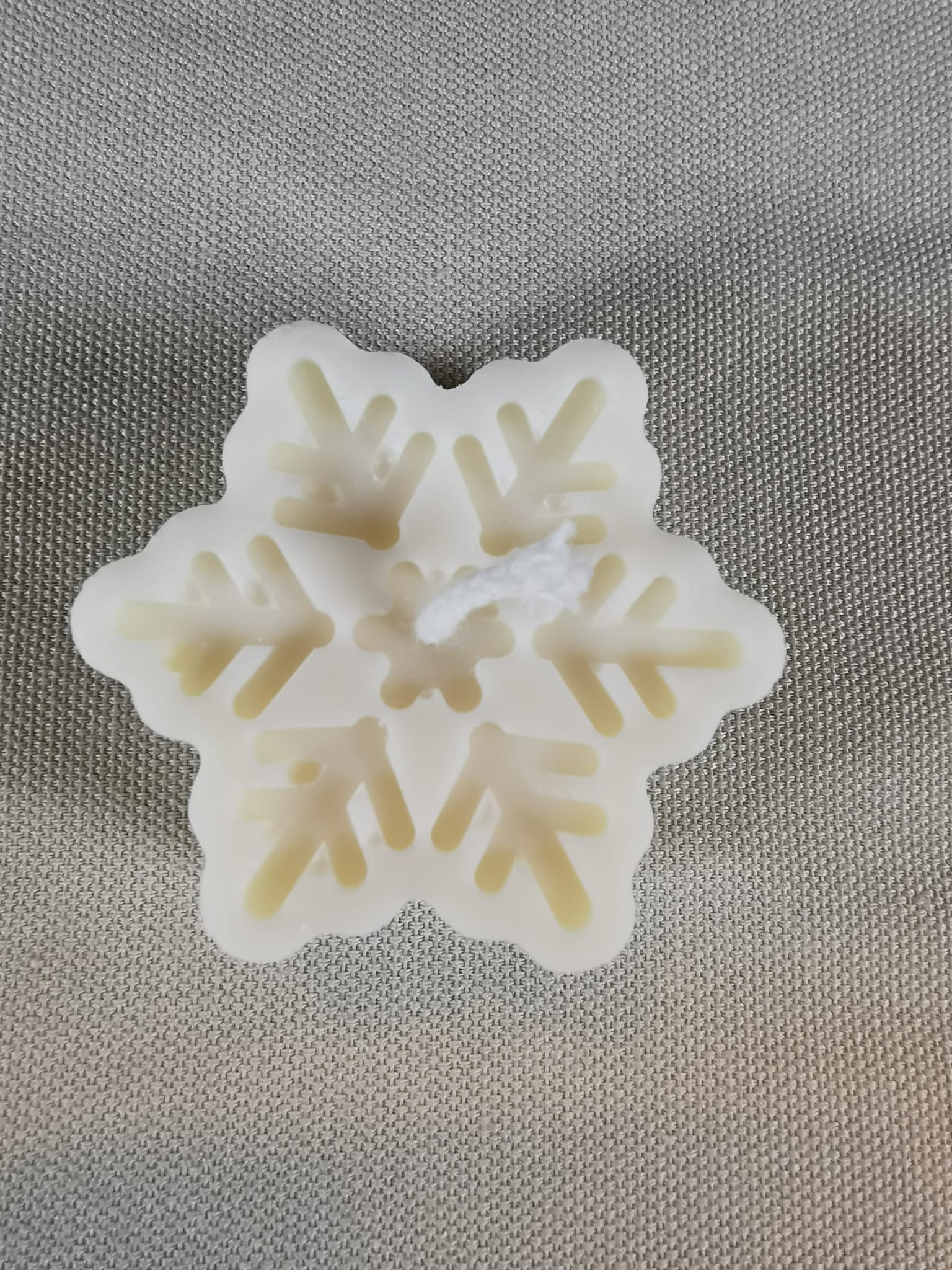 Handgefertigte Schneeflocken-Kerze aus naturreinem Rapswachs in zartem Cremeweiß, winterliche Deko auf Stoffuntergrund