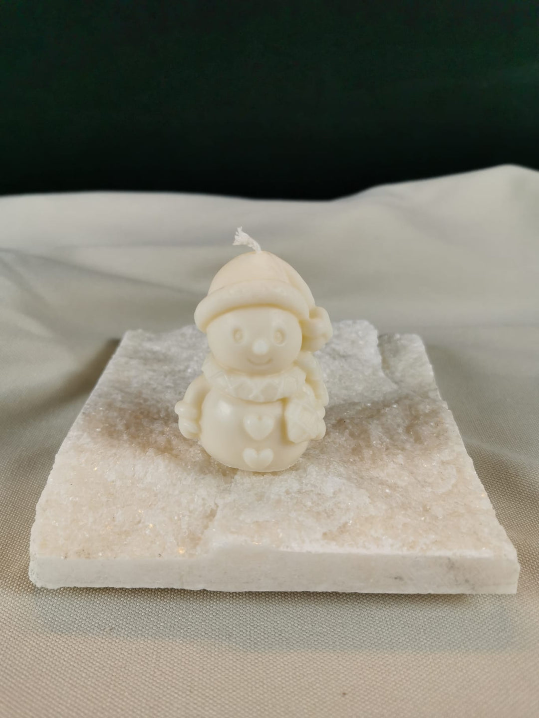 Handgegossene Schneemann-Figurenkerze aus hellem Rapswachs, mit Mütze, Schal und Herzdetails, auf einer glitzernden Steinplatte präsentiert.