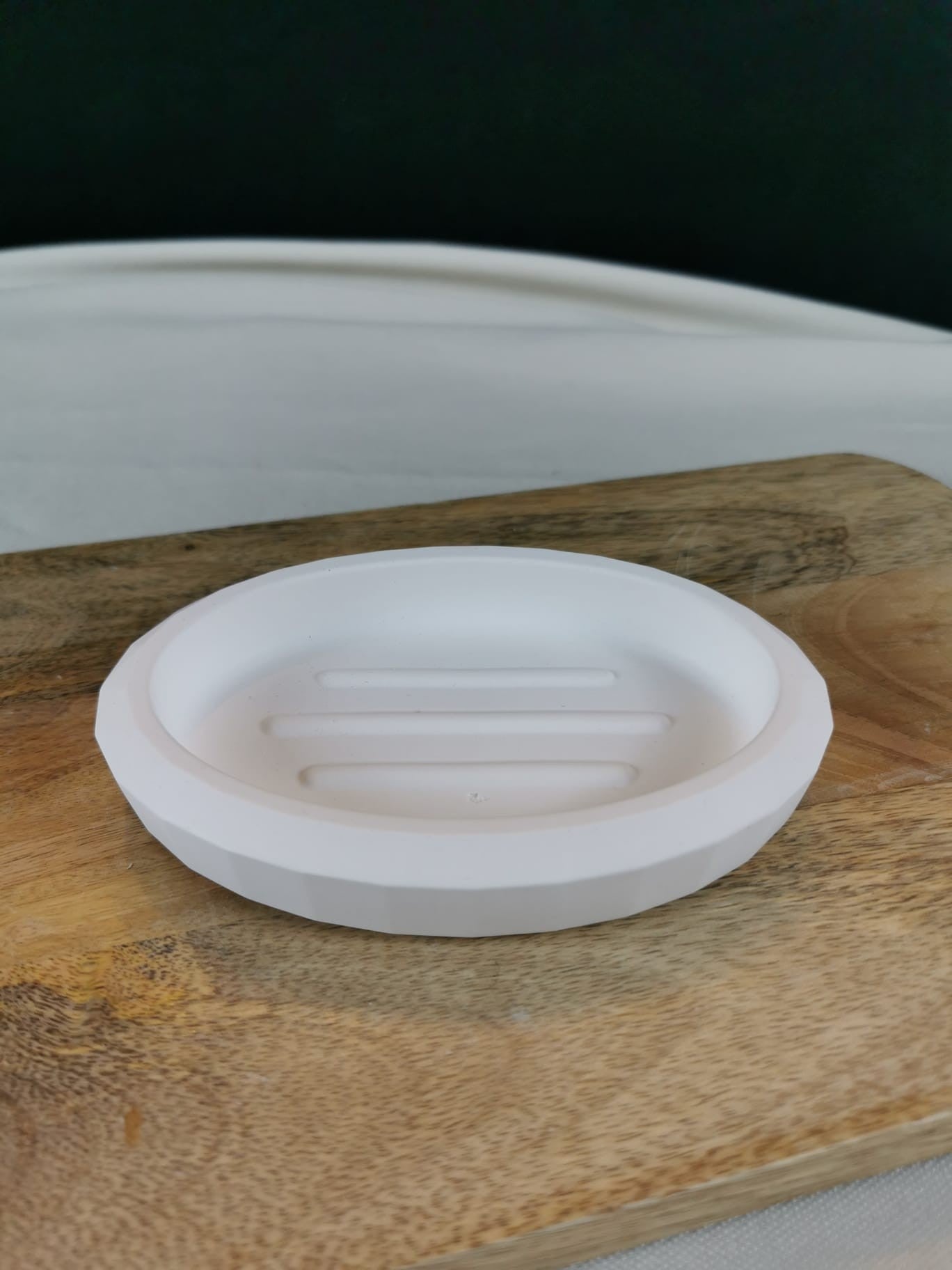 „Runde weiße Seifenschale mit Ablaufrillen auf Holzuntergrund – moderne handgefertigte Seifenablage.“