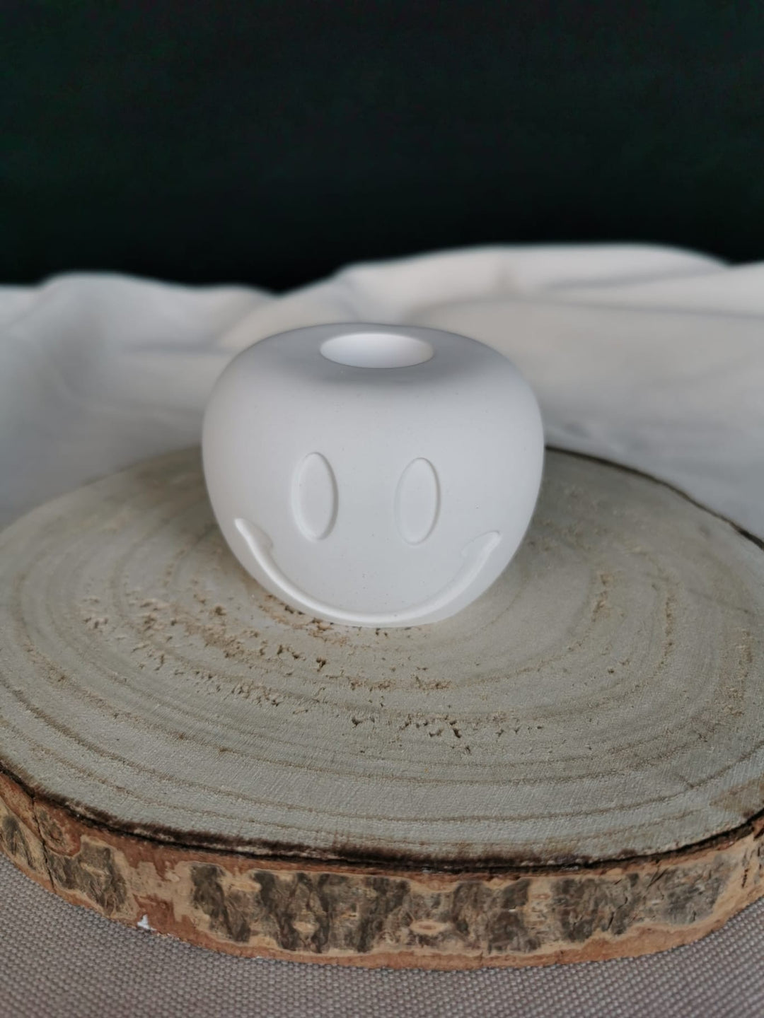 Weißer, handgefertigter Smiley-Kerzenhalter aus Keramik, auf Holzuntergrund platziert – modernes Wohnaccessoire mit positiver Ausstrahlung.
