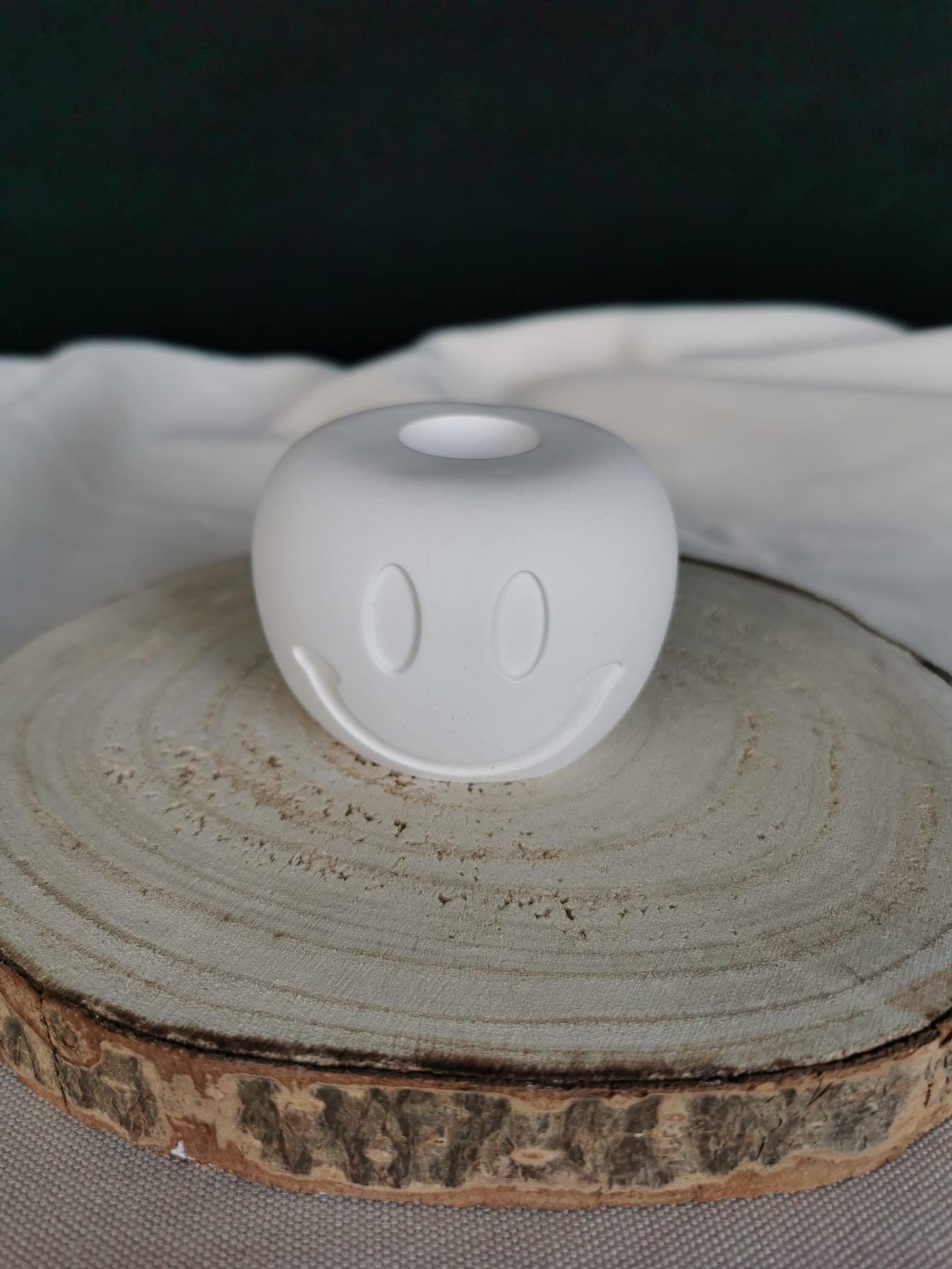 Weißer, handgefertigter Smiley-Kerzenhalter aus Keramik, auf Holzuntergrund platziert – modernes Wohnaccessoire mit positiver Ausstrahlung.