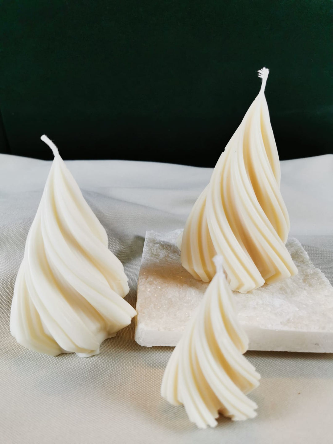 Handgegossene spiralförmige Weihnachtsbaum-Kerze aus hellem Bio-Rapswachs, auf einer glitzernden Steinplatte präsentiert.