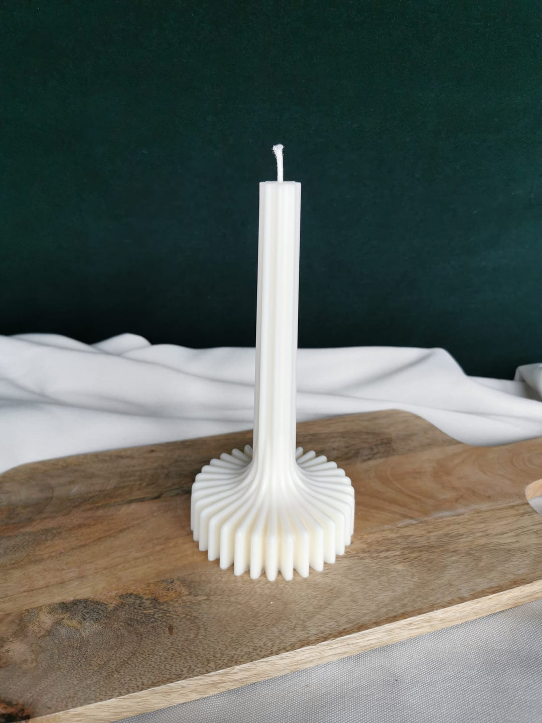 „Handgegossene weiße Stabkerze mit dekorativem wellenförmigem Fuß aus Rapswachs auf Holzbrett“