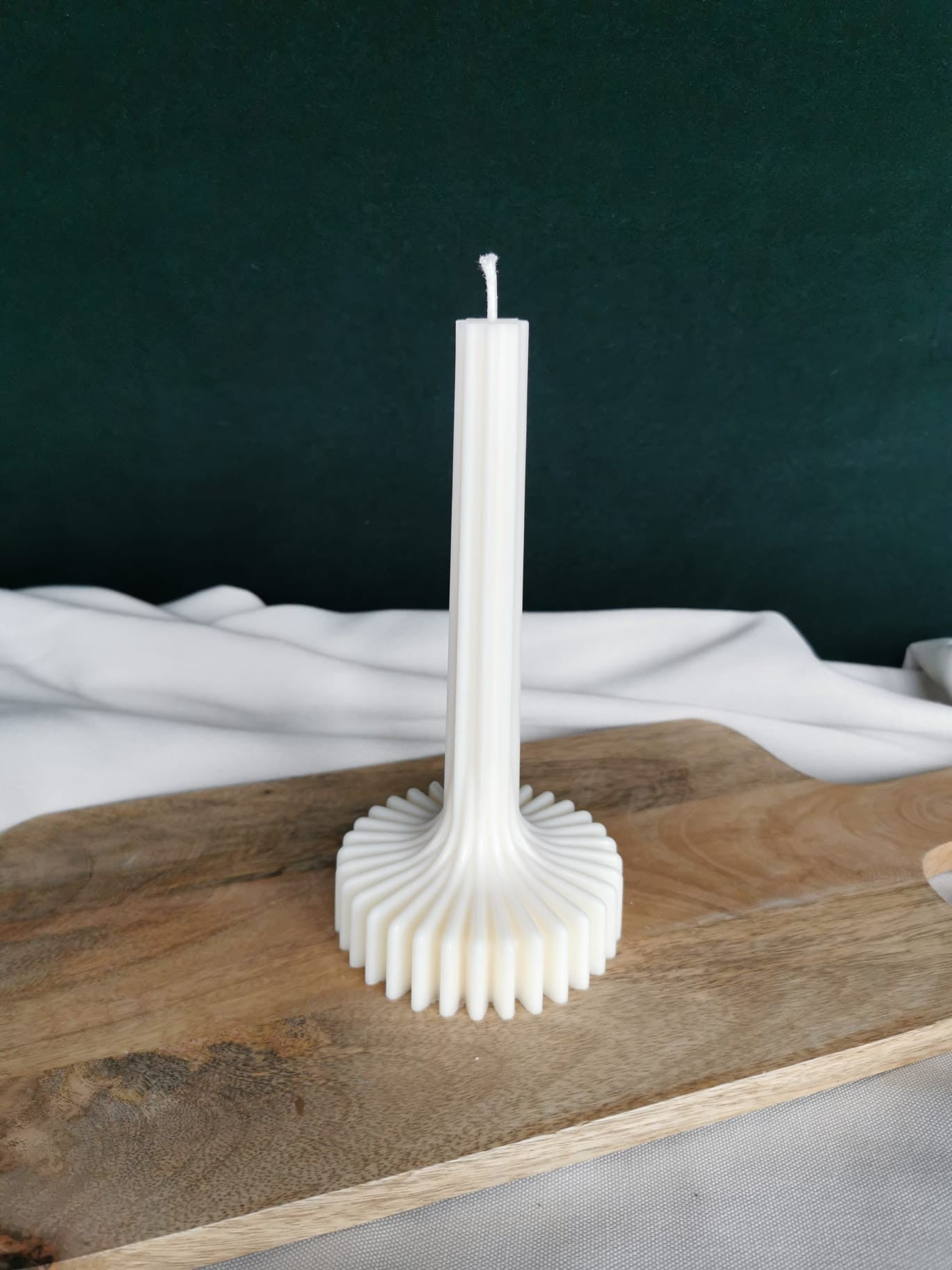 „Handgegossene weiße Stabkerze mit dekorativem wellenförmigem Fuß aus Rapswachs auf Holzbrett“