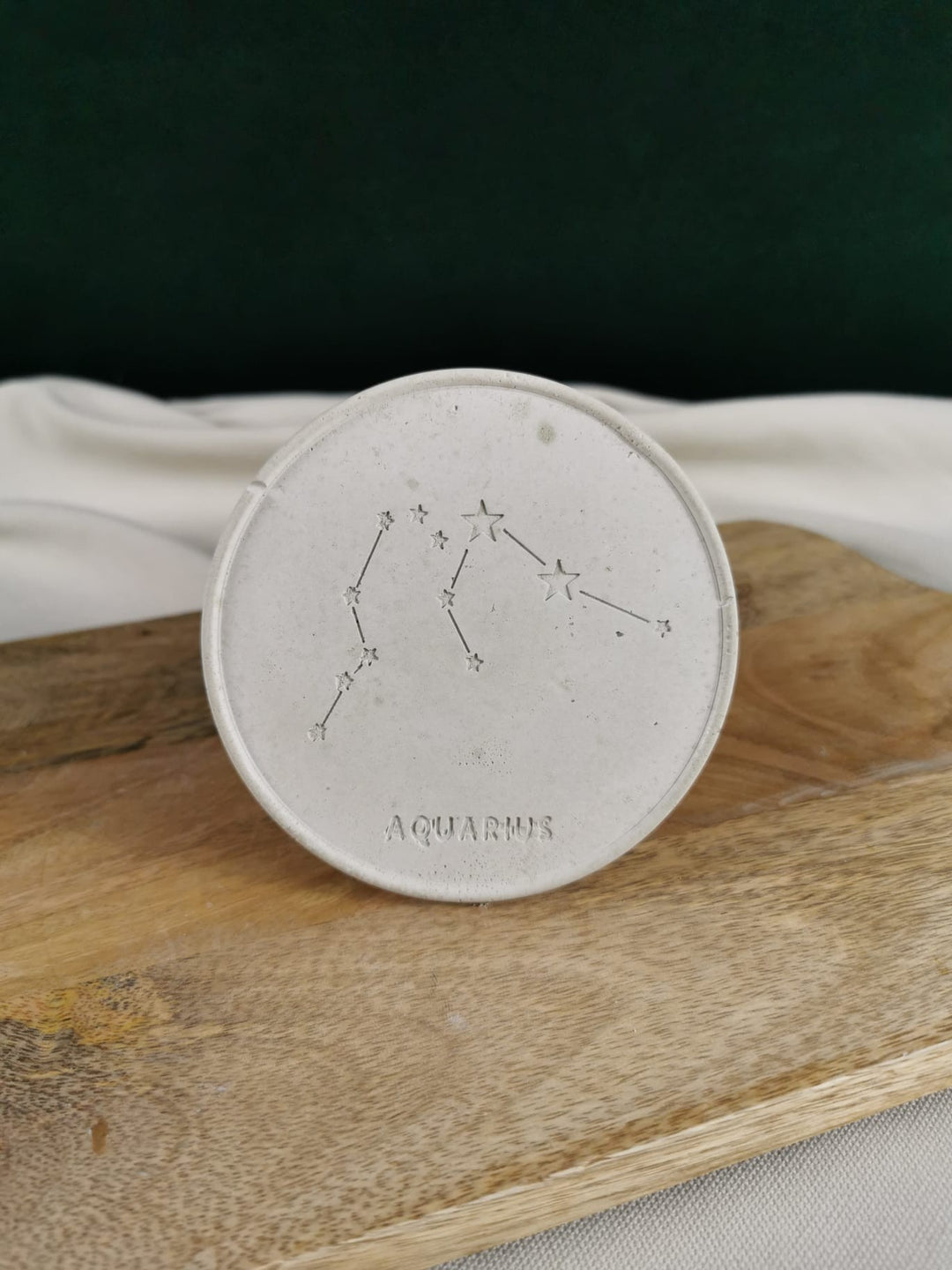 „Runder handgefertigter Beton-Untersetzer mit eingraviertem Aquarius/Wassermann Sternzeichen, fotografiert auf einem Holzbrett.“
