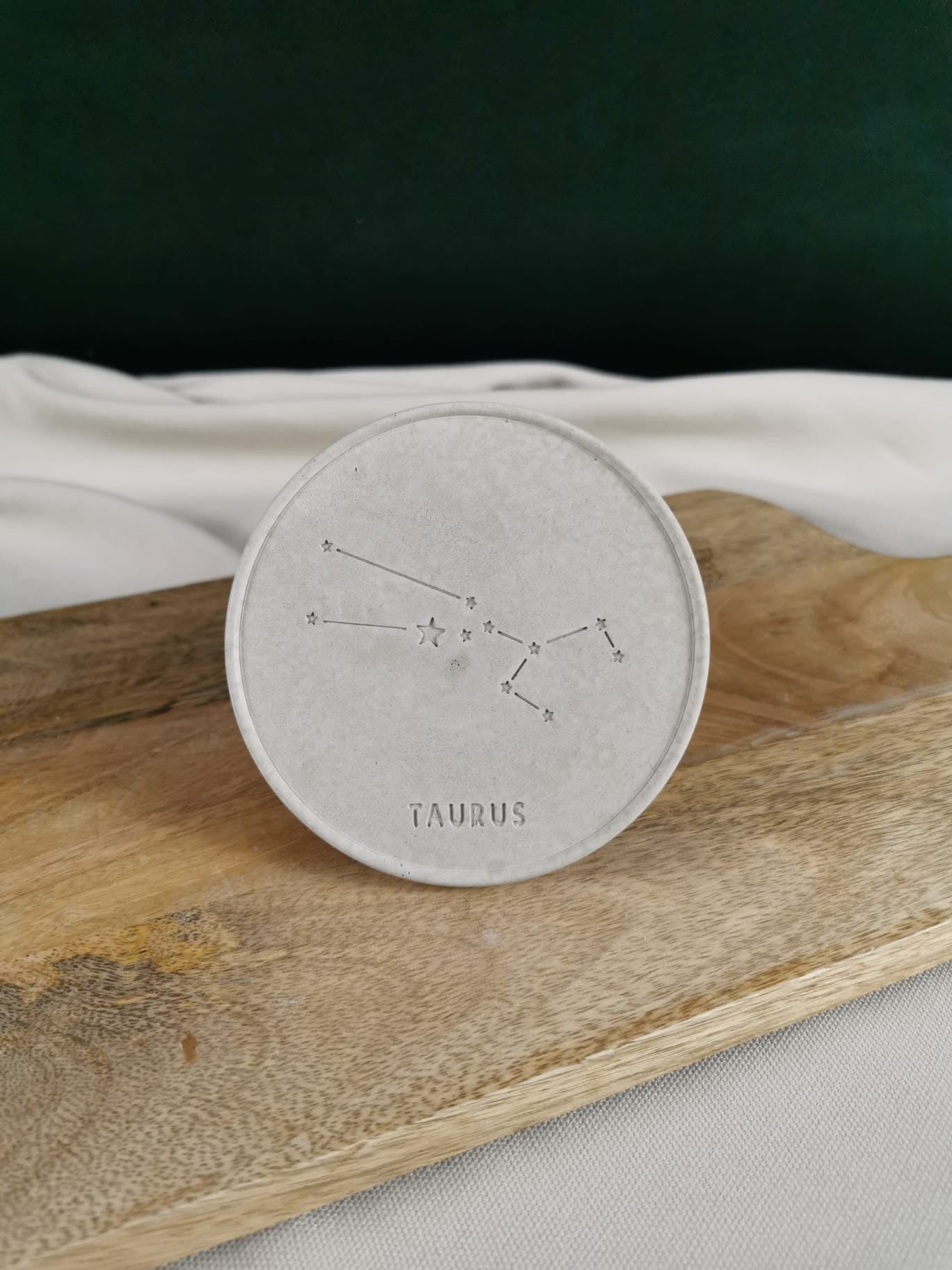 „Handgemachter runder Beton-Untersetzer mit eingraviertem Taurus-Sternbild auf Holzunterlage“