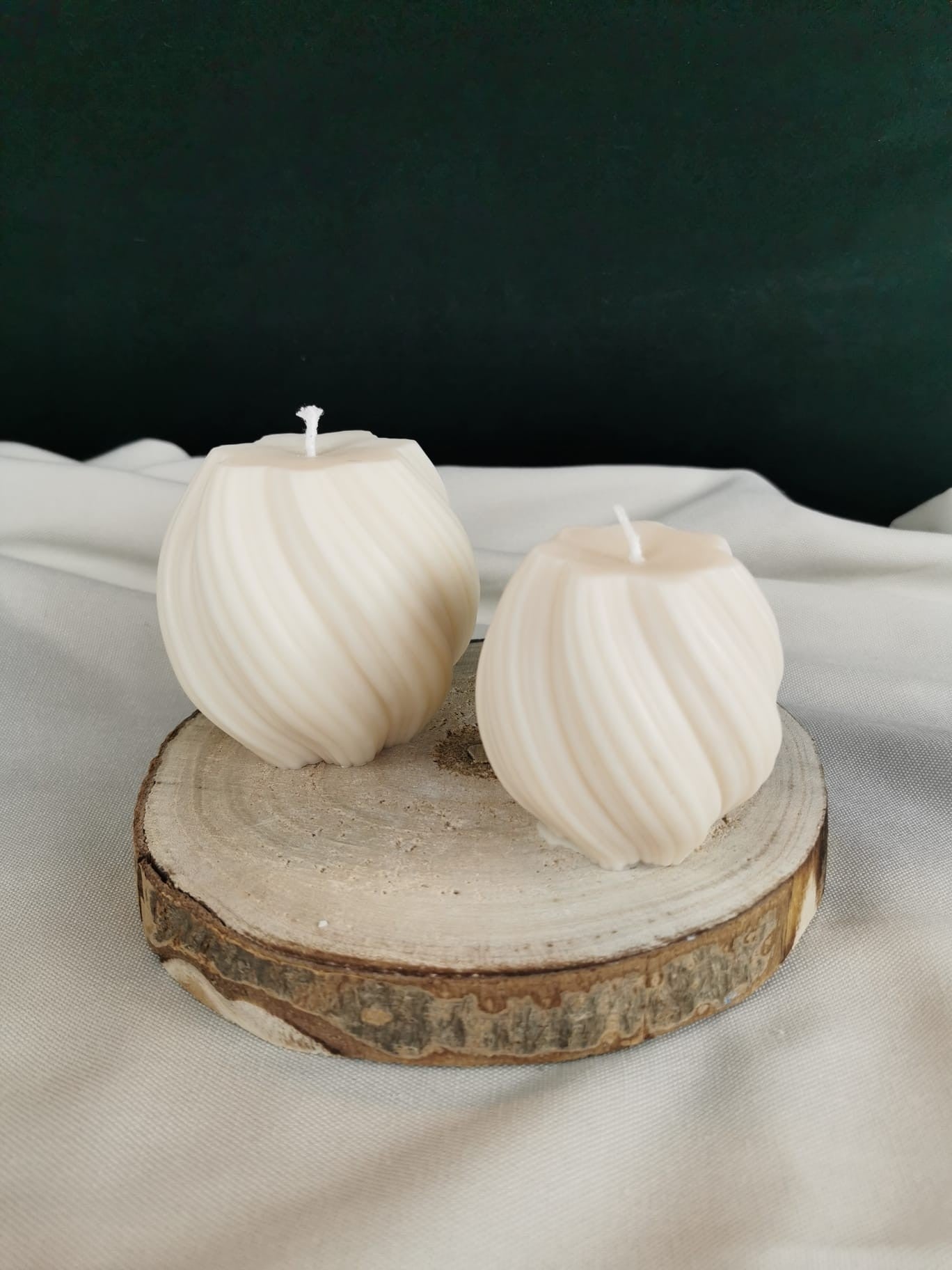 Zwei handgemachte, cremefarbene Swirl-Kugelkerzen aus Rapswachs auf einer Holzscheibe – dekorative, moderne Kerzen für gemütliche Wohnakzente.
