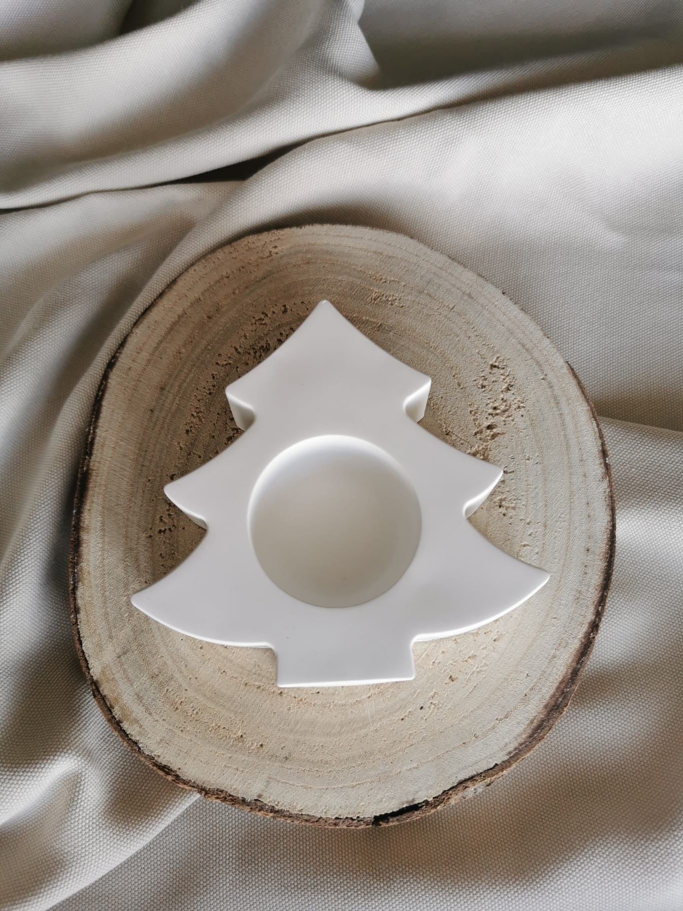 Weißer Kerzenhalter in Tannenbaumform aus Gießkeramik, dekorativ auf einer Holzscheibe präsentiert.