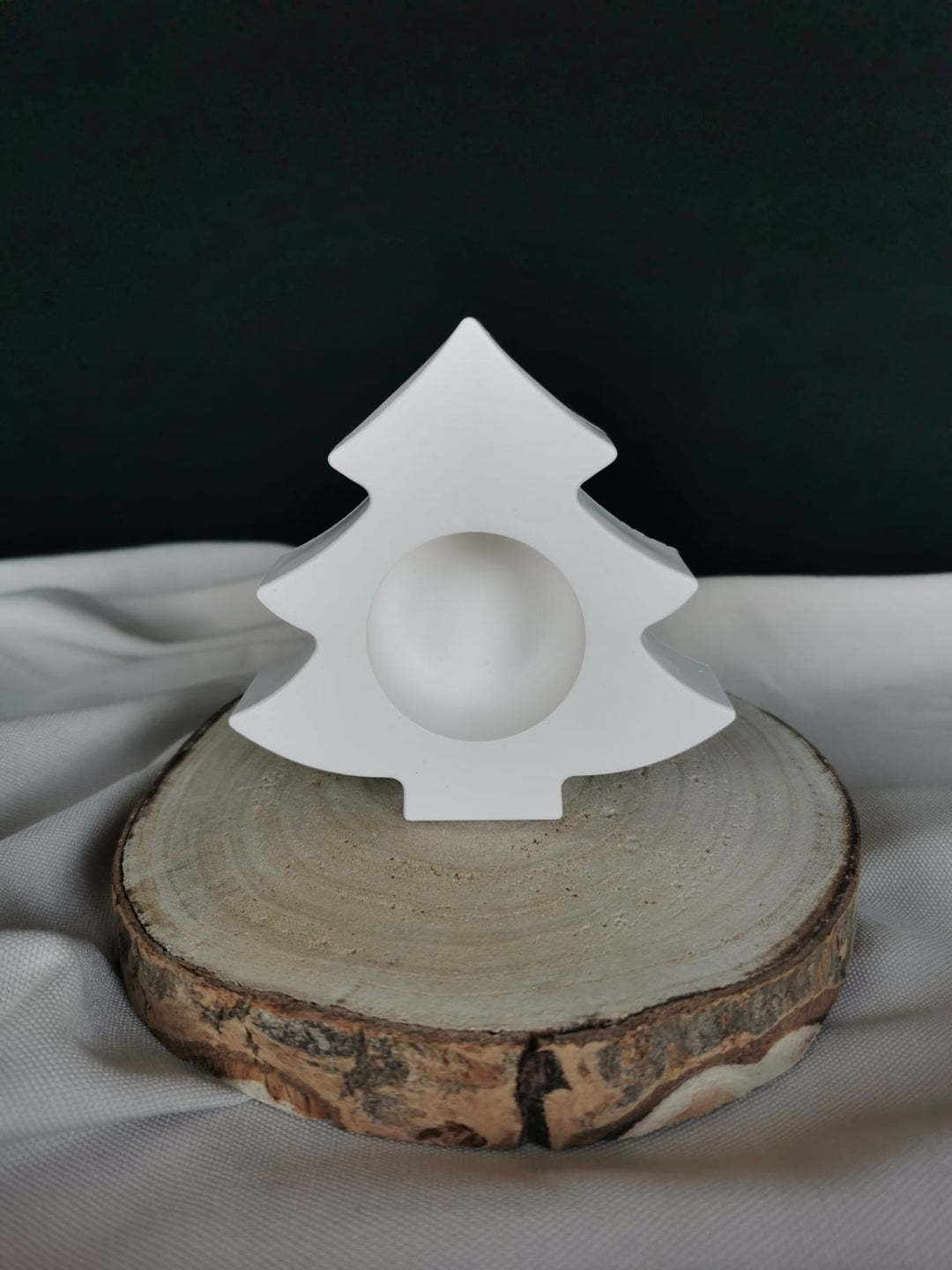 Weißer Kerzenhalter in Tannenbaumform aus Gießkeramik, dekorativ auf einer Holzscheibe präsentiert.