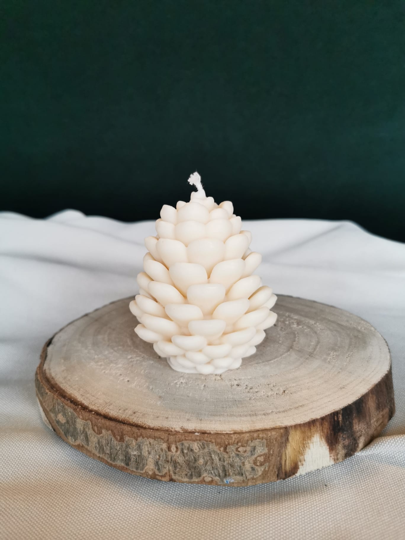 Handgemachte Tannenzapfen-Kerze aus naturfarbenem Rapswachs, dekorativ auf einer Holzscheibe präsentiert.
