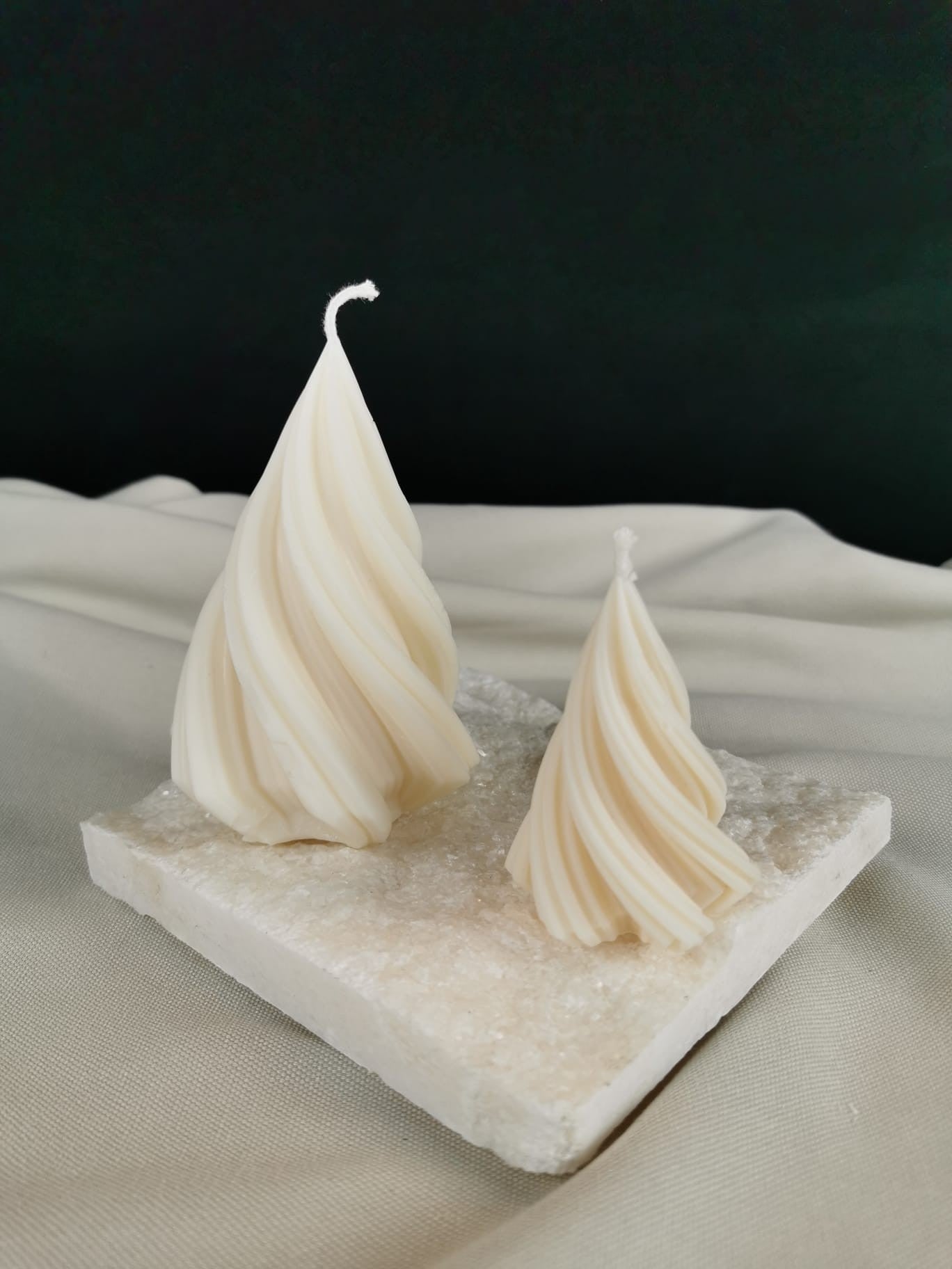 „Handgegossene Rapswachskerzen im gedrehten Tannenbaum-Design – festliche Deko in Cremeweiß auf Steinplatte.“