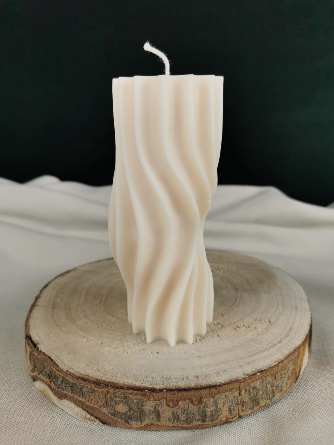„Handgegossene cremefarbene Säulenkerze aus Rapswachs mit geschwungener Wellenstruktur, dekorativ auf einem Holzbrett präsentiert.“