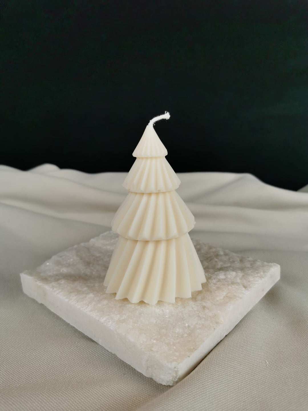 „Handgegossene Weihnachtsbaum-Kerze aus veganem Rapswachs mit eleganter gefächerter Struktur in Cremeweiß auf natürlicher Steinplatte.“