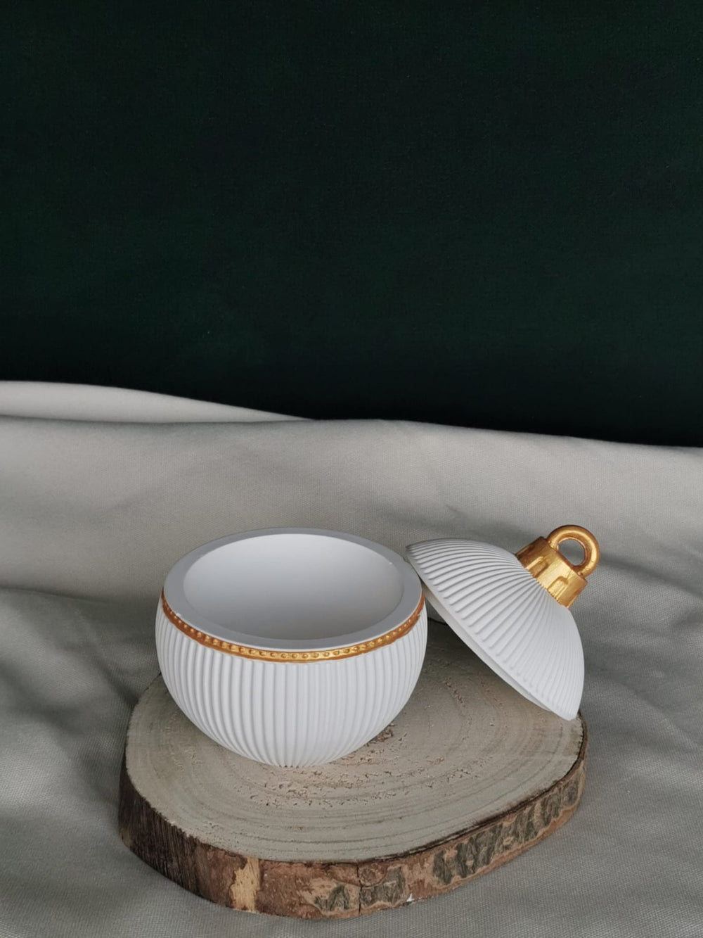 „Geöffnete weiße Keramikkugel mit goldenen Details und Rillenstruktur, handgefertigt, als edle Weihnachtsdekoration oder Aufbewahrungsdose – stilvoll platziert auf Holzscheibe.“