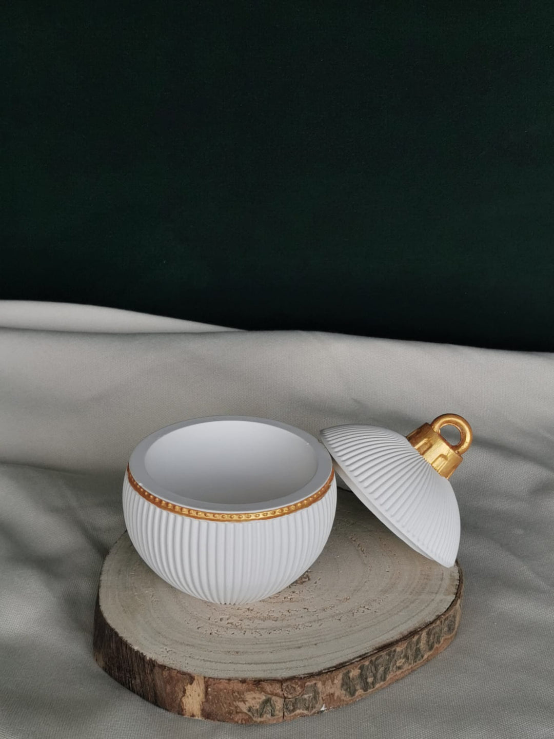 „Geöffnete weiße Keramikkugel mit goldenen Details und Rillenstruktur, handgefertigt, als edle Weihnachtsdekoration oder Aufbewahrungsdose – stilvoll platziert auf Holzscheibe.“